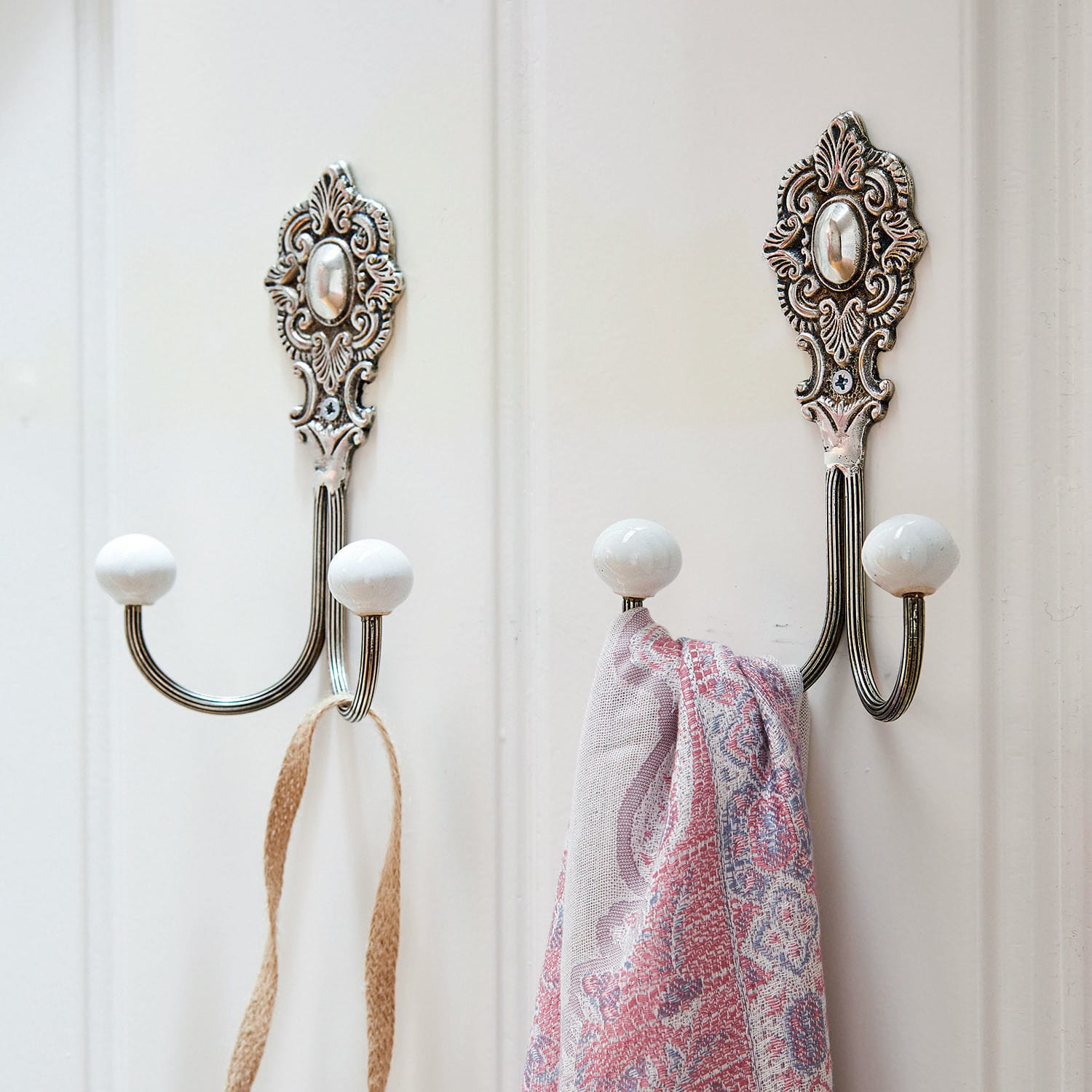 Metalowy wieszak ścienny z białymi ceramicznymi końcówkami i ozdobną podstawą do domu
