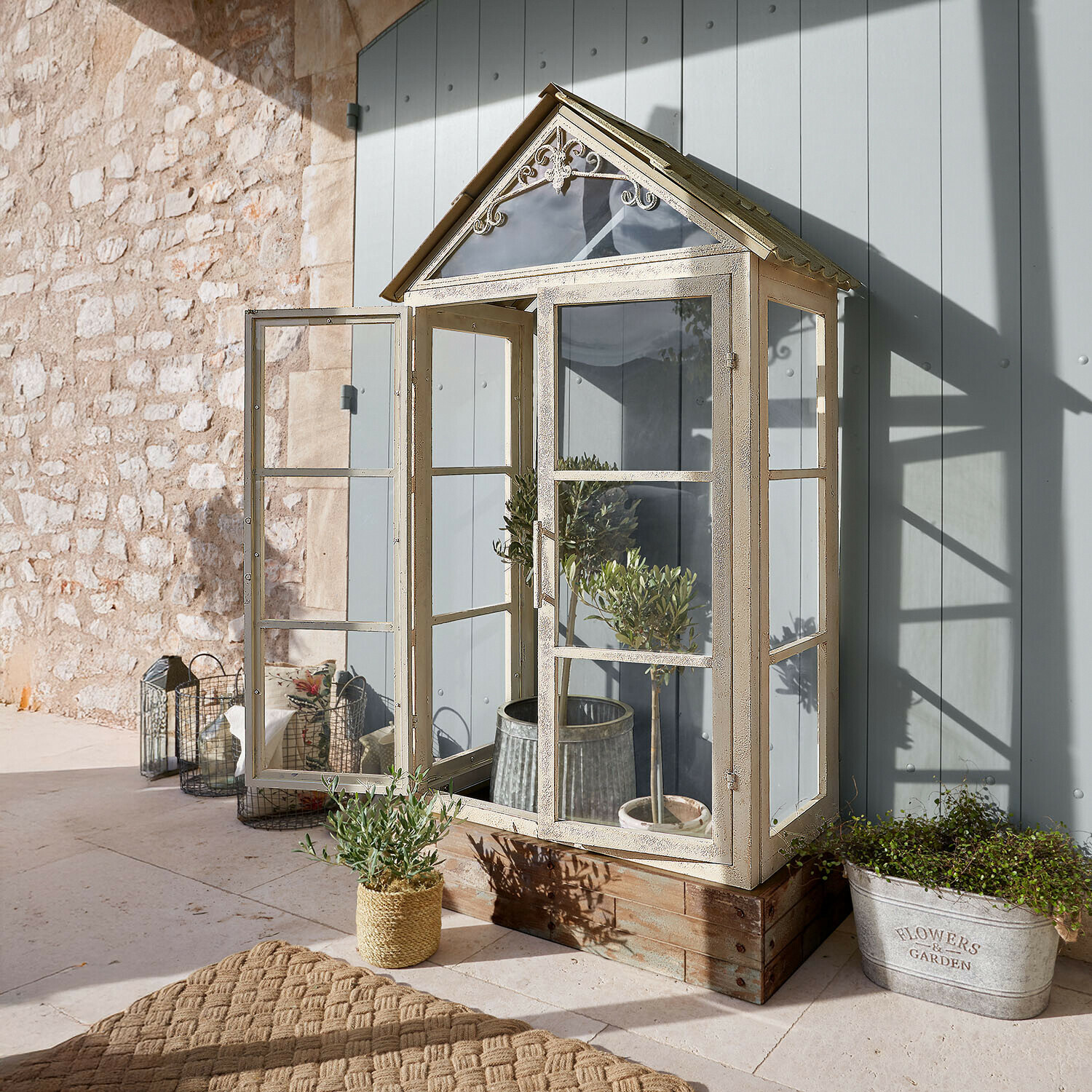 Mała szklarnia ogrodowa z metalową ramą w kolorze kremowym na drewnianej podstawie do uprawy roślin