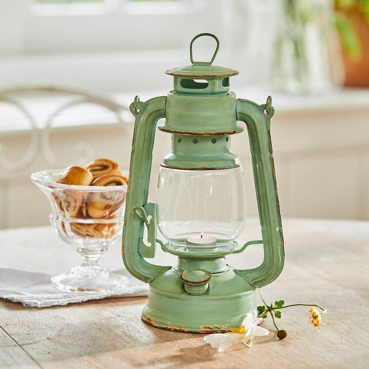 Lampion Clemence Zielona metalowa latarnia z efektem postarzenia na drewnianym stole z ciastkami w tle
