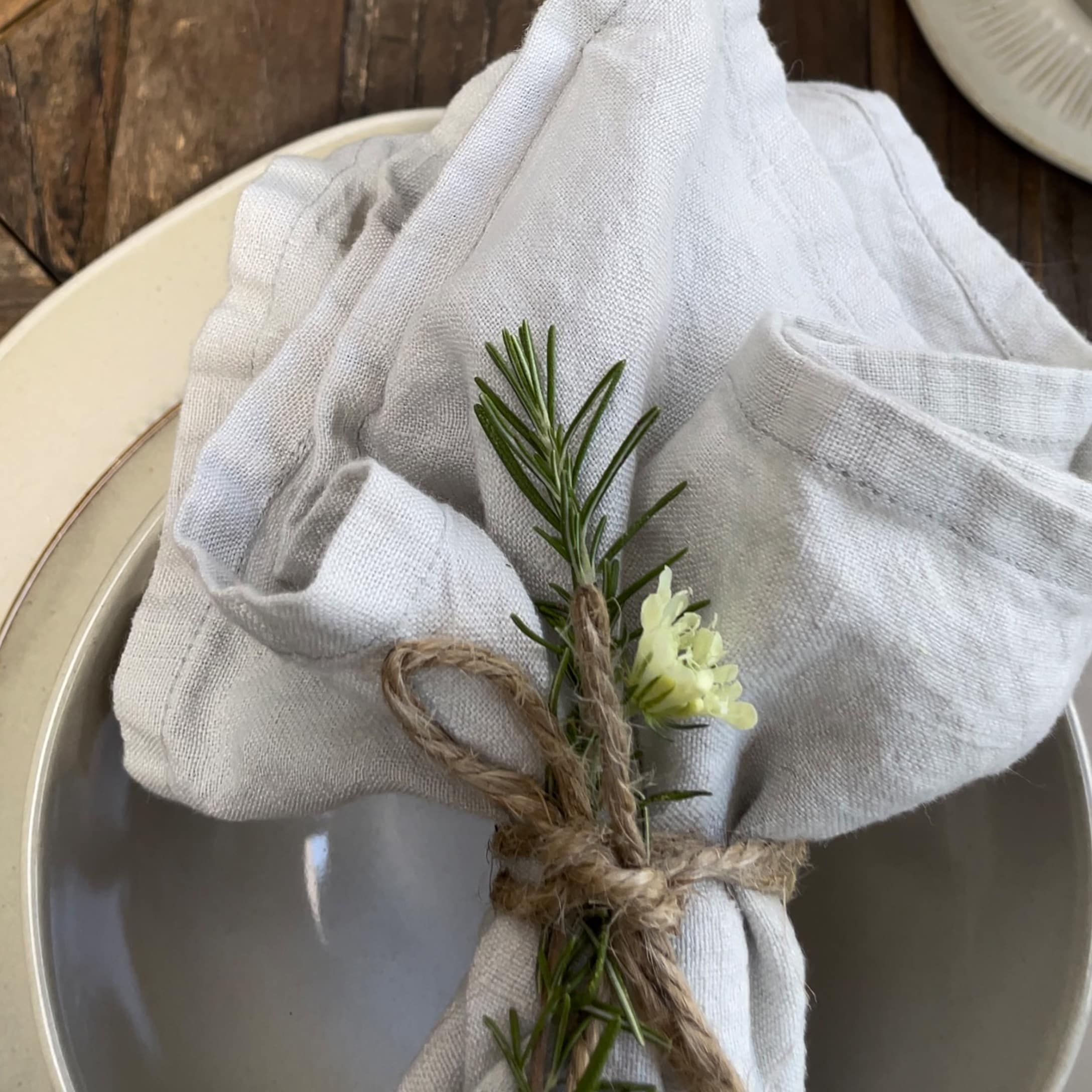 Lniany biały obrus z dekoracją z gałązki rozmarynu i kwiatem na talerzu, styl rustykalny