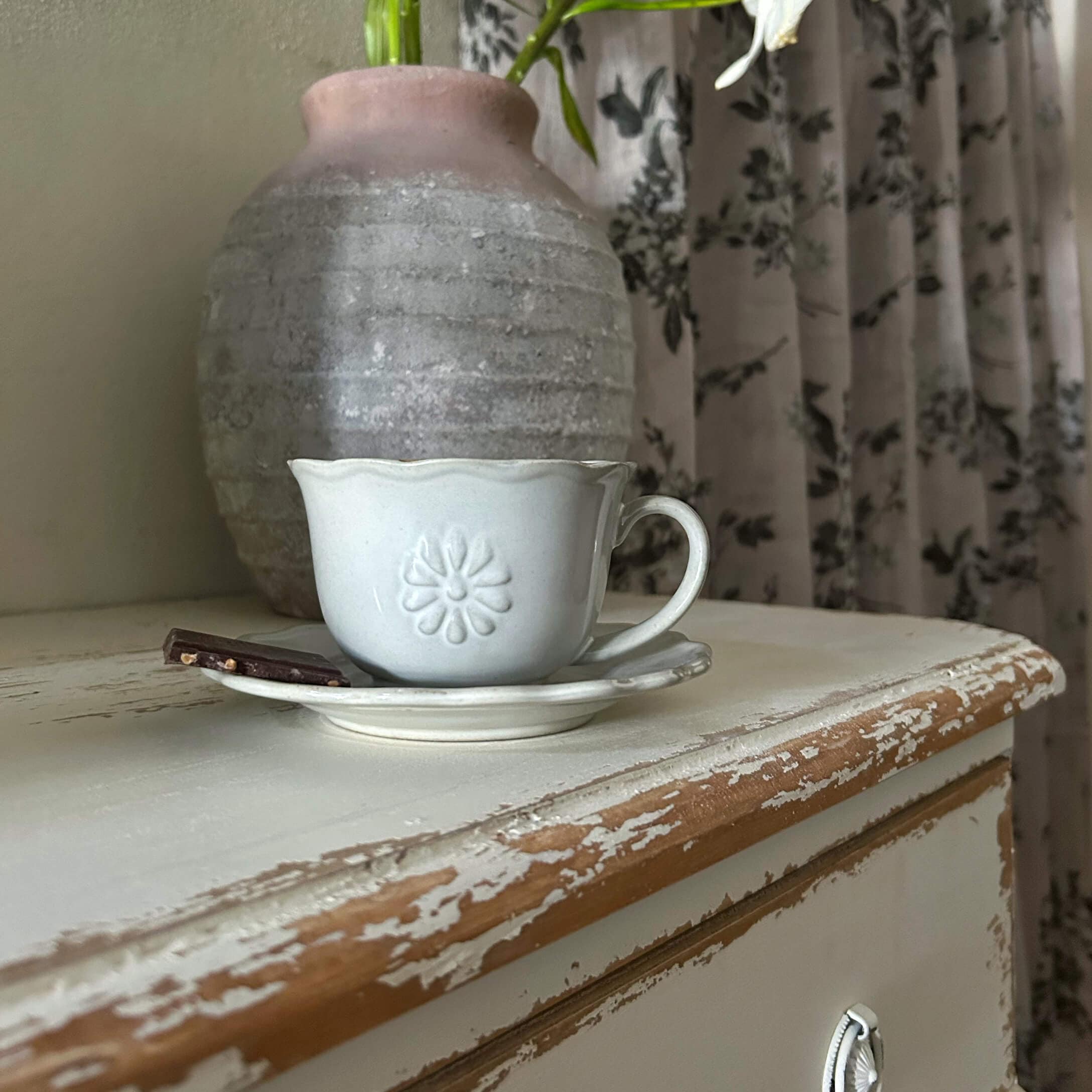 Biała ceramiczna filiżanka z talerzykiem i kawałkiem czekolady na postarzałym drewnianym blacie