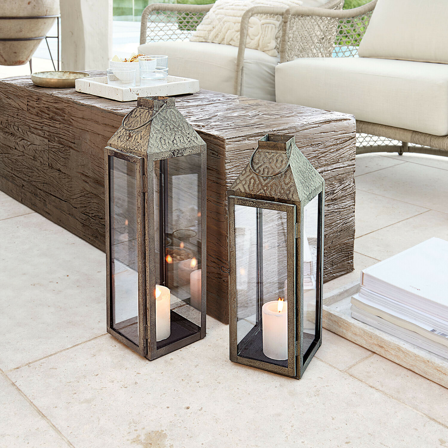 Dwie metalowe lampiony z szybami i białymi świecami na jasnej podłodze w nowoczesnym salonie