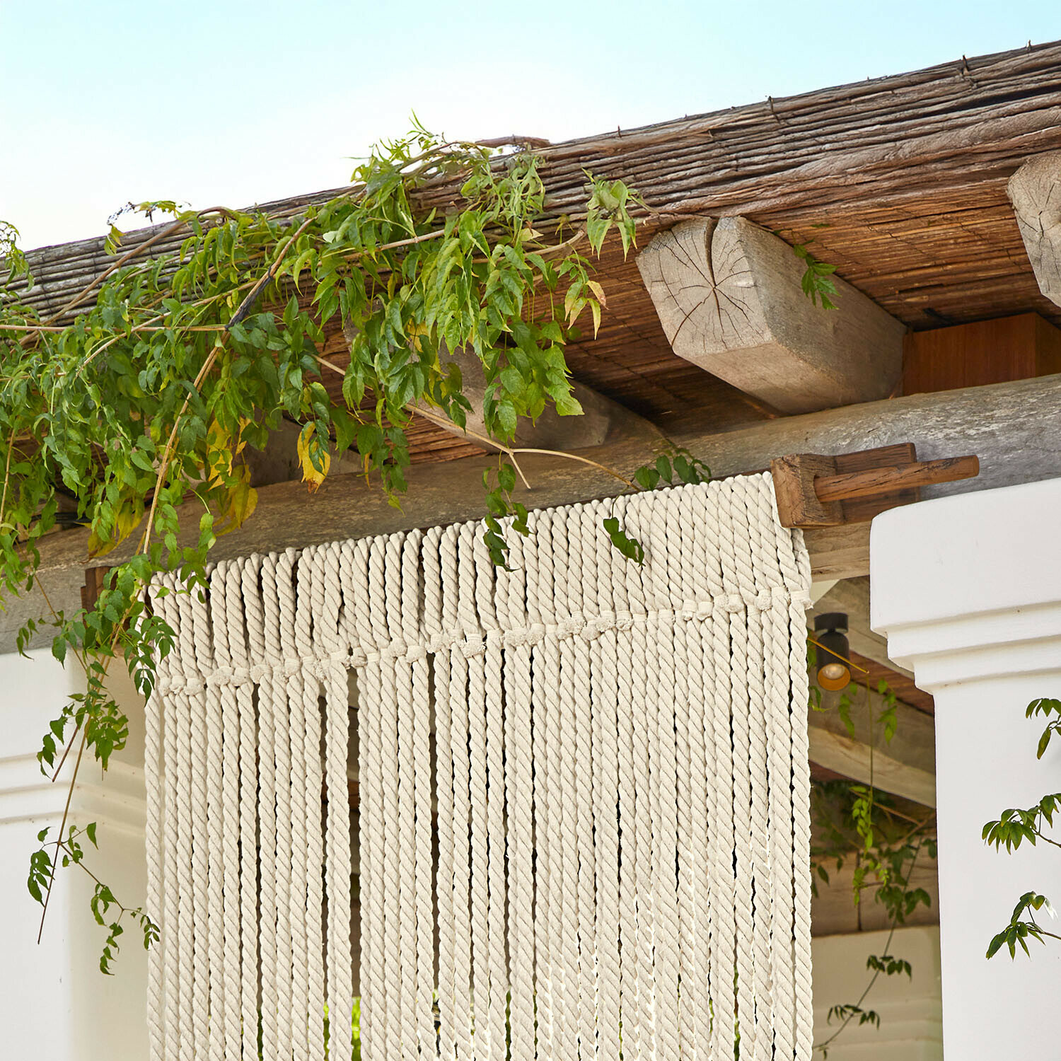 Dekoracyjna zasłona z białej bawełnianej liny na drewnianej konstrukcji z zielonymi liśćmi