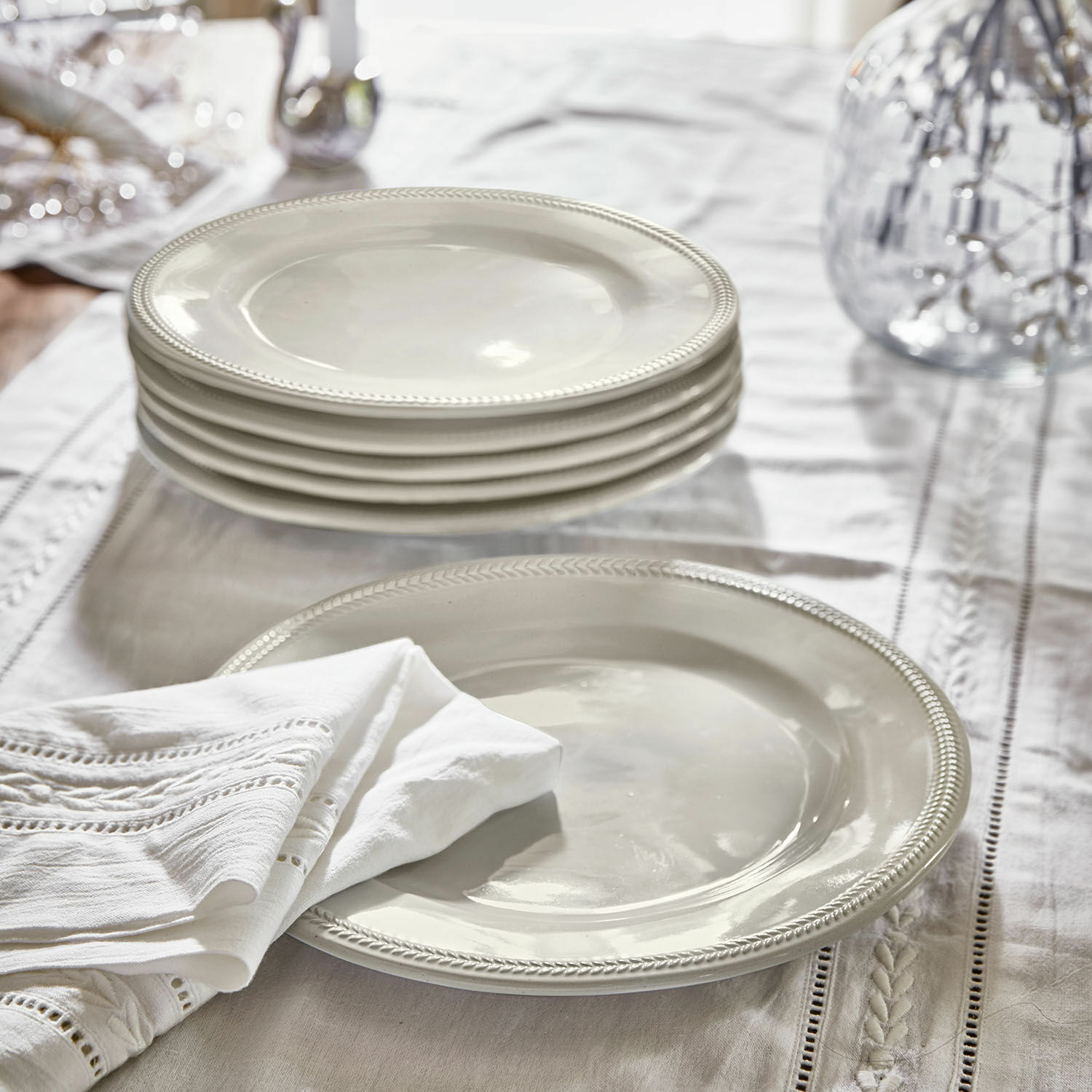 Zestaw białych ceramicznych talerzy z ozdobnym brzegiem na lnianym obrusie, dekoracja stołu