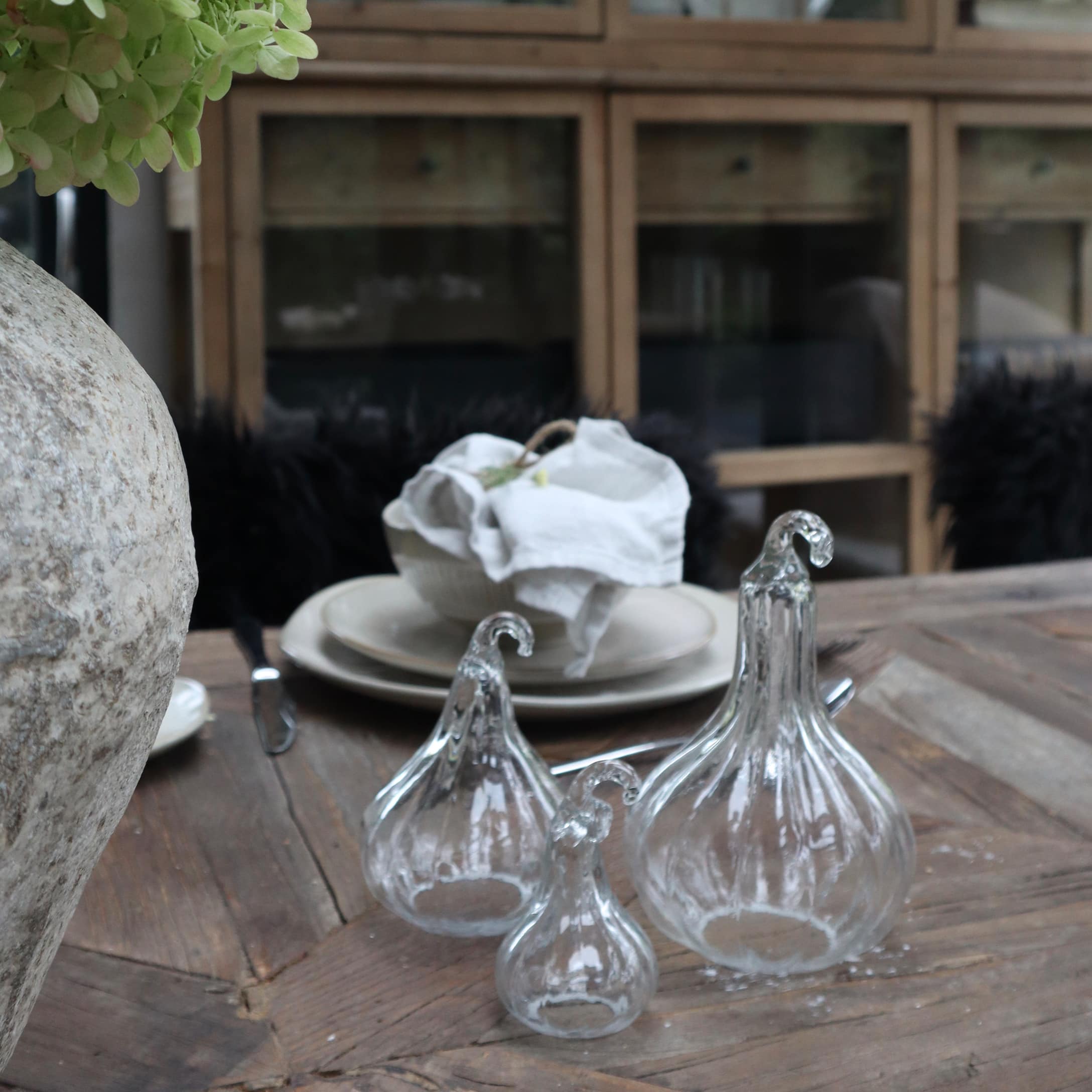 Trzy przezroczyste szklane dekoracje w kształcie dyni na drewnianym stole w rustykalnym wnętrzu