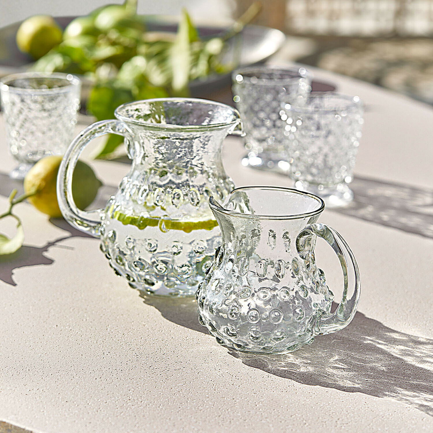 Szklany dzbanek i dzbanuszek z wypukłym wzorem na jasnym stole, idealne do napojów na lato