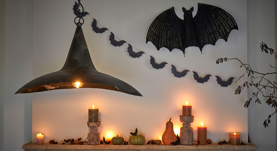 Dekoracja halloweenowa z czarnymi lampami, świecami i girlandą nietoperzy na jasnej ścianie