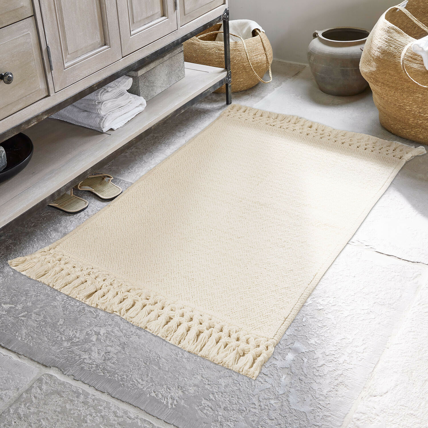 Beżowy dywanik bawełniany z frędzlami na kamiennej podłodze w łazience, dekoracja wnętrza