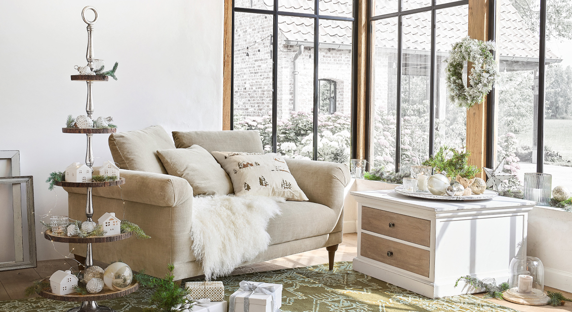 Przytulny salon w stylu wiejskim z beżową sofą, białą komodą i świąteczną dekoracją zimową