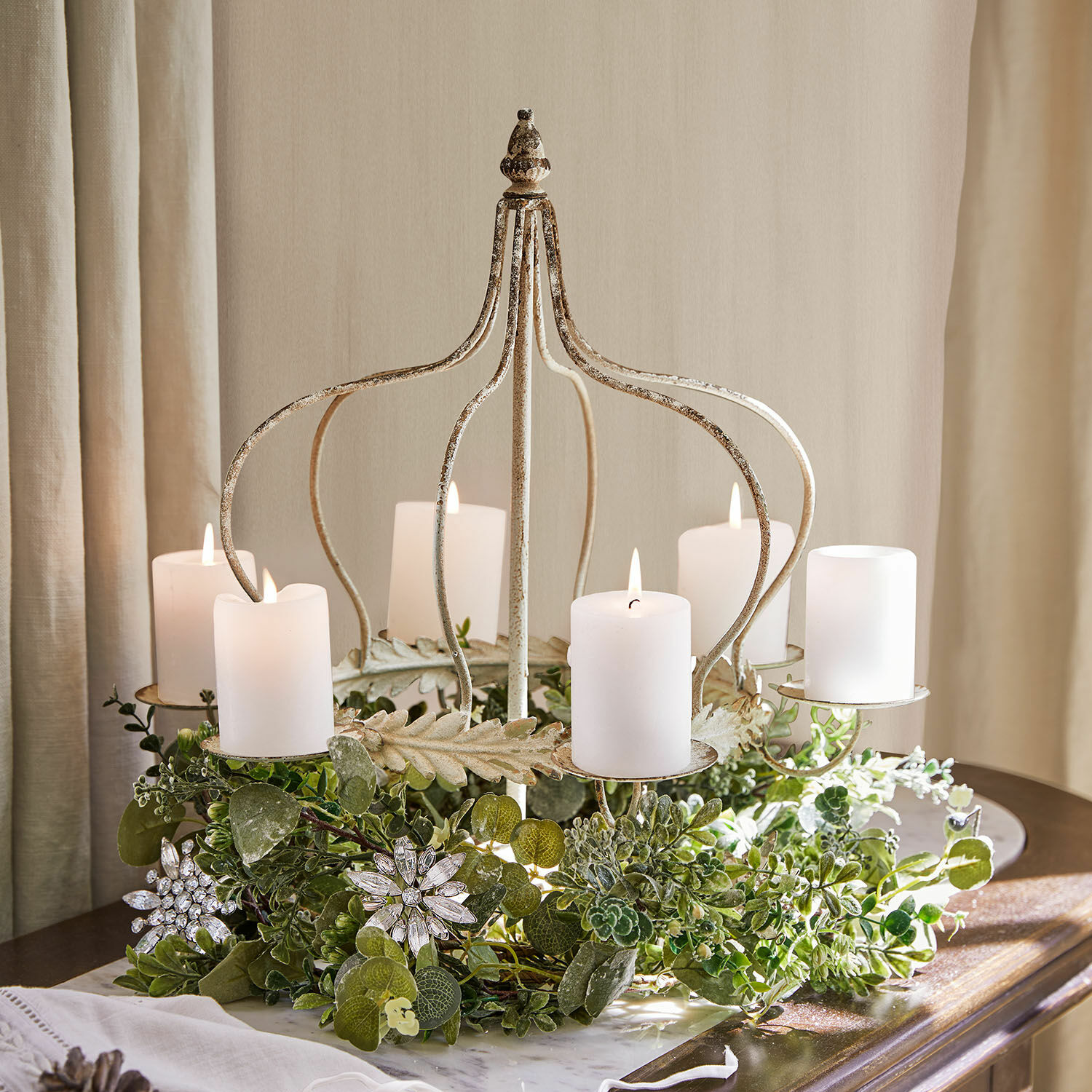 Świecznik Traventa Metalowy świecznik w kształcie korony z białymi świecami i zielonymi dekoracjami na stole