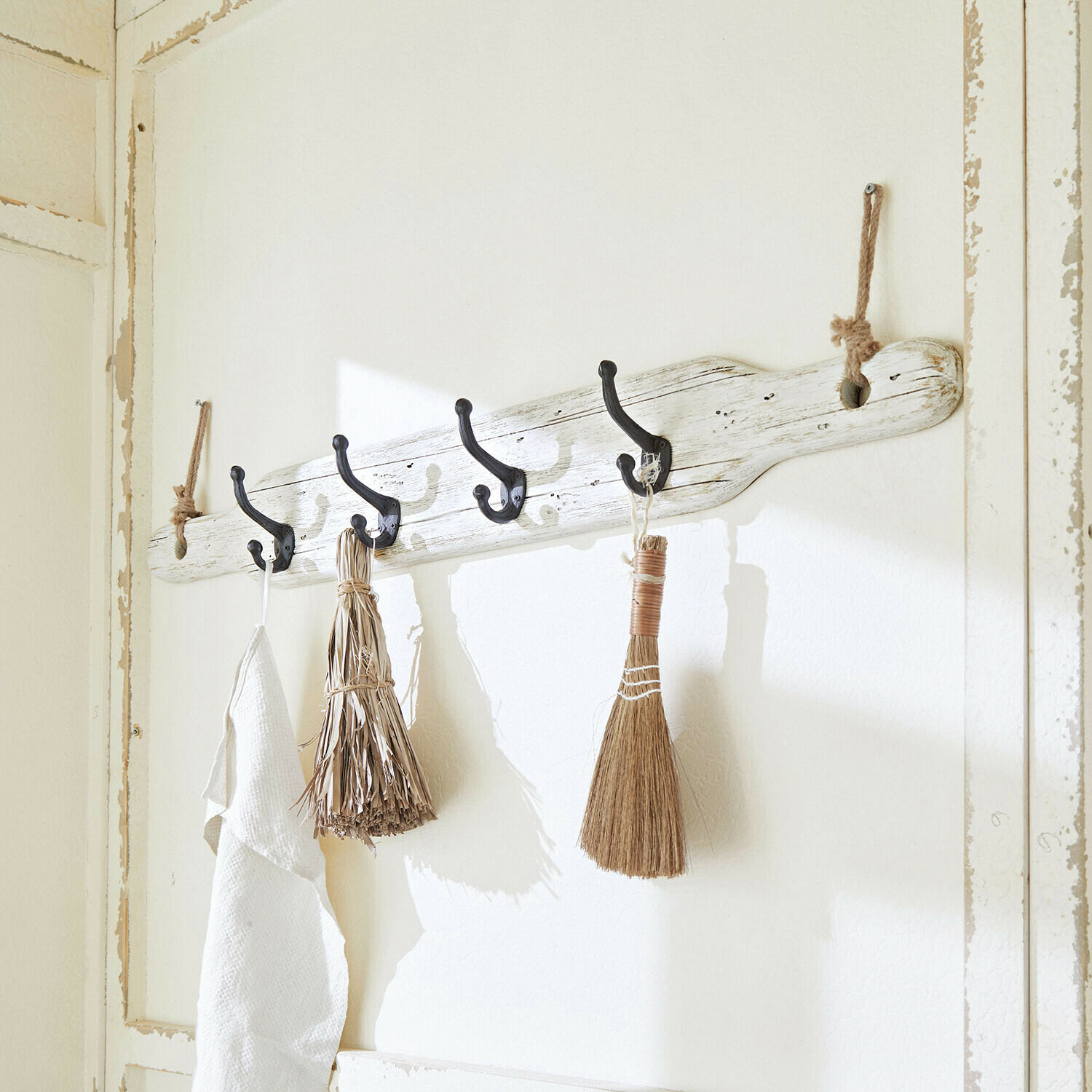 Rustykalny wieszak ścienny z drewna w białym kolorze z czarnymi hakami i naturalnymi szczotkami do dekoracji