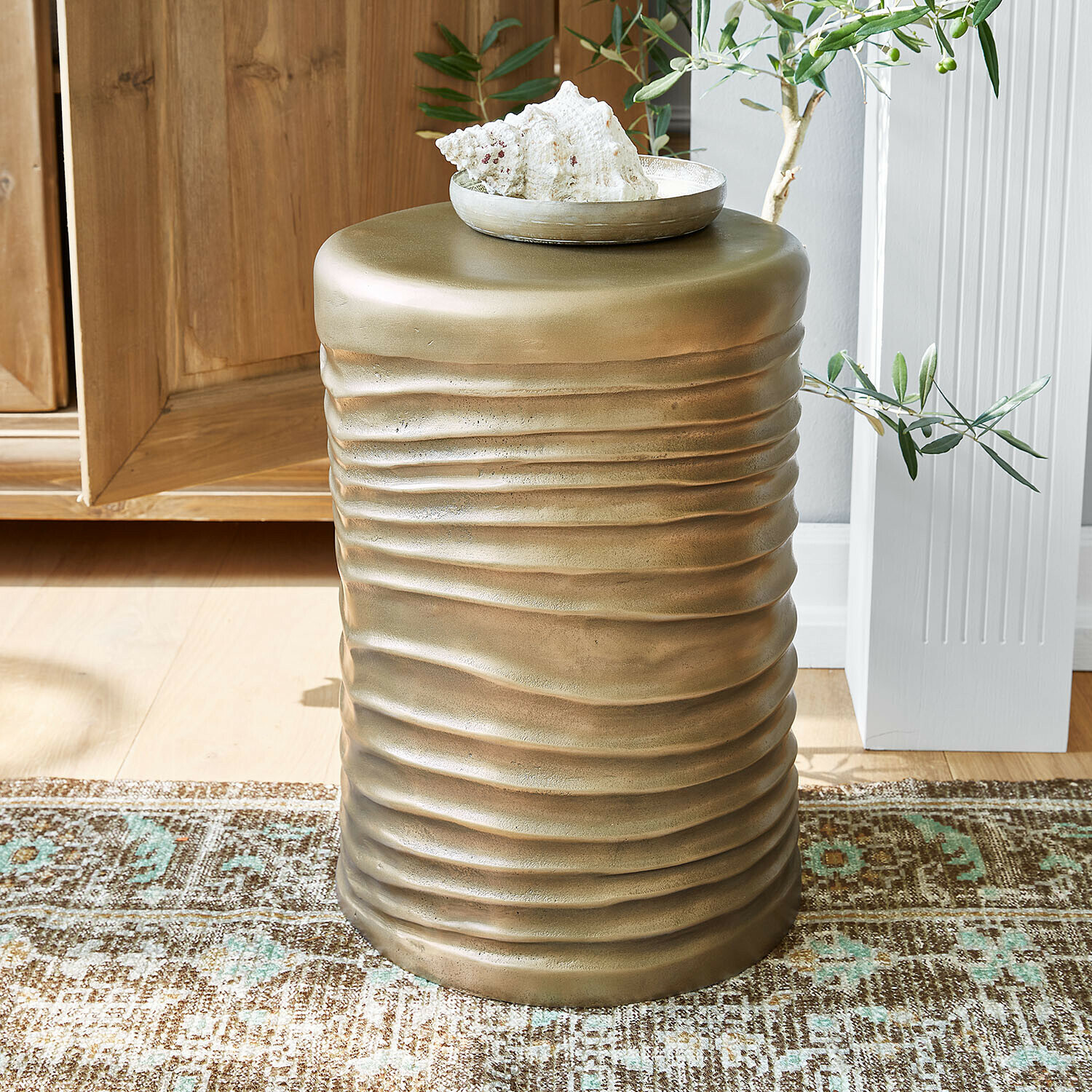 Złoty metalowy stolik boczny z falistą fakturą na dywanie w jasnym wnętrzu