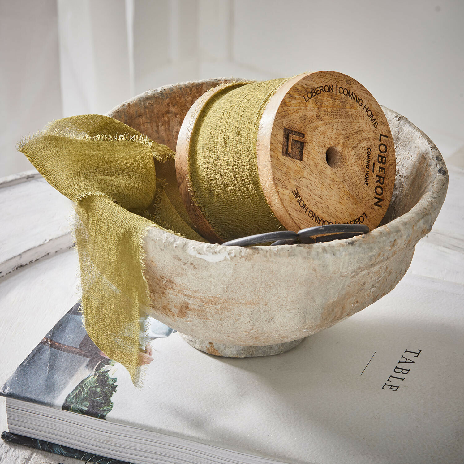 Naturalna miska z kamienia z zieloną tkaniną i drewnianą szpulką na książce o tematyce stołu