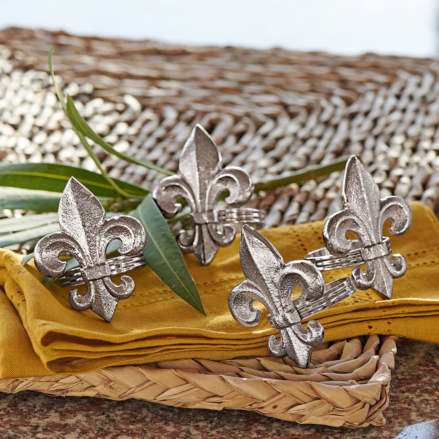 Obrączka na serwetki, zestaw 4 szt. Fleur De Lis Metalowe srebrne pierścienie na serwetki z motywem lilii na żółtej tkaninie i wiklinowym podkładzie
