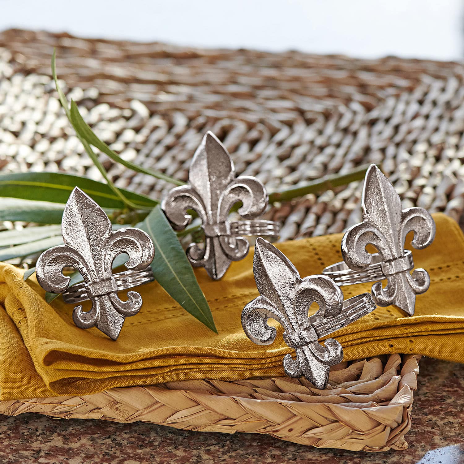 Obrączka na serwetki, zestaw 4 szt. Fleur De Lis Metalowe srebrne pierścienie na serwetki z motywem lilii na żółtej tkaninie i wiklinowym podkładzie