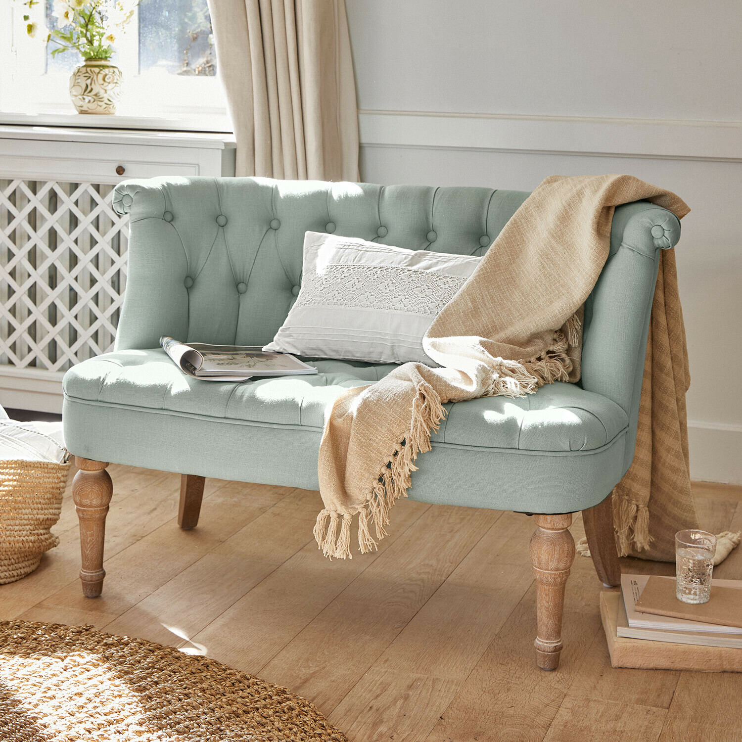 Sofa Weralin Miętowa tapicerowana sofa z drewnianymi nogami, ozdobiona beżowym kocem i białą poduszką, styl vintage