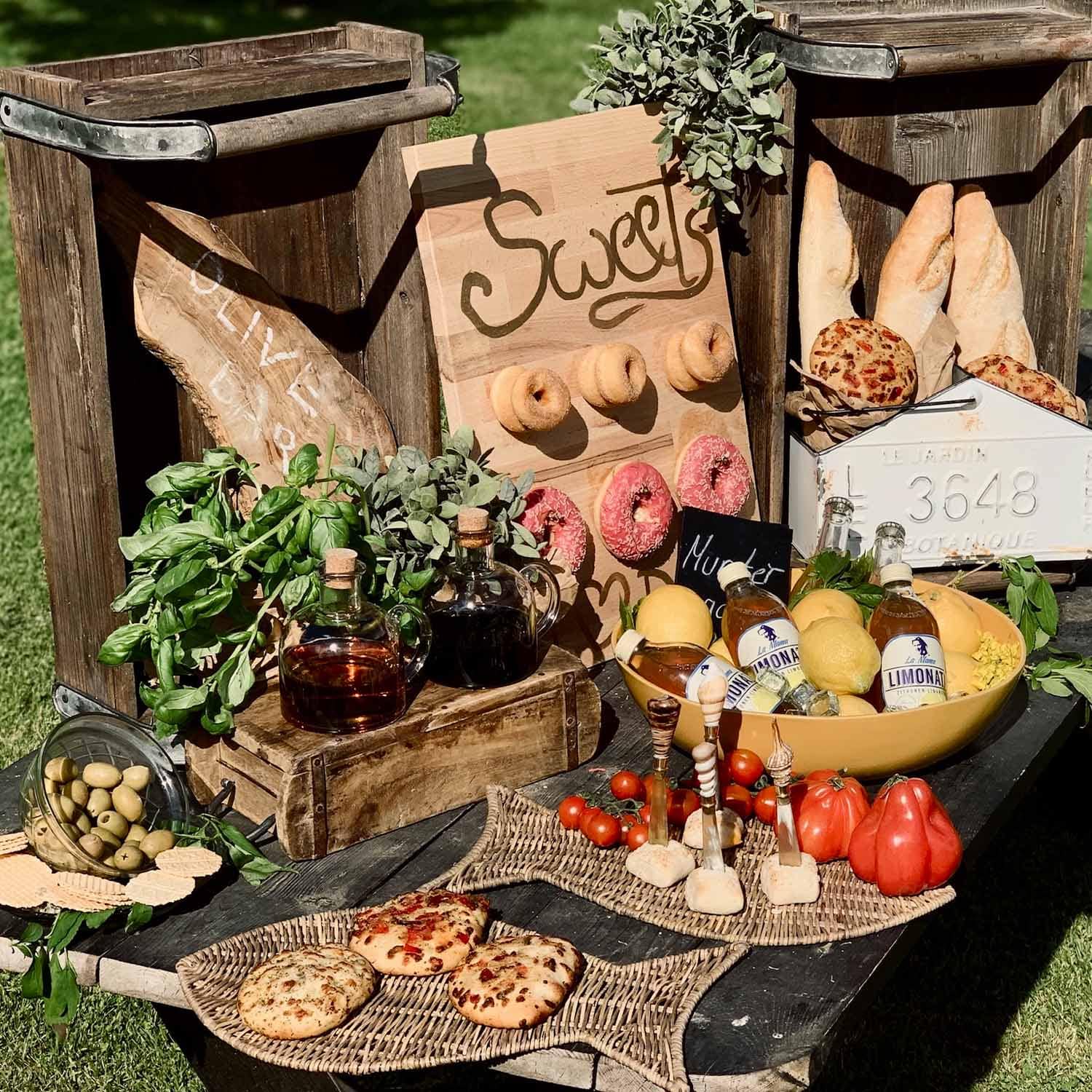 Rustykalny stół z drewnianymi skrzynkami, pieczywem, oliwkami, ziołami i lemoniadą na zewnątrz