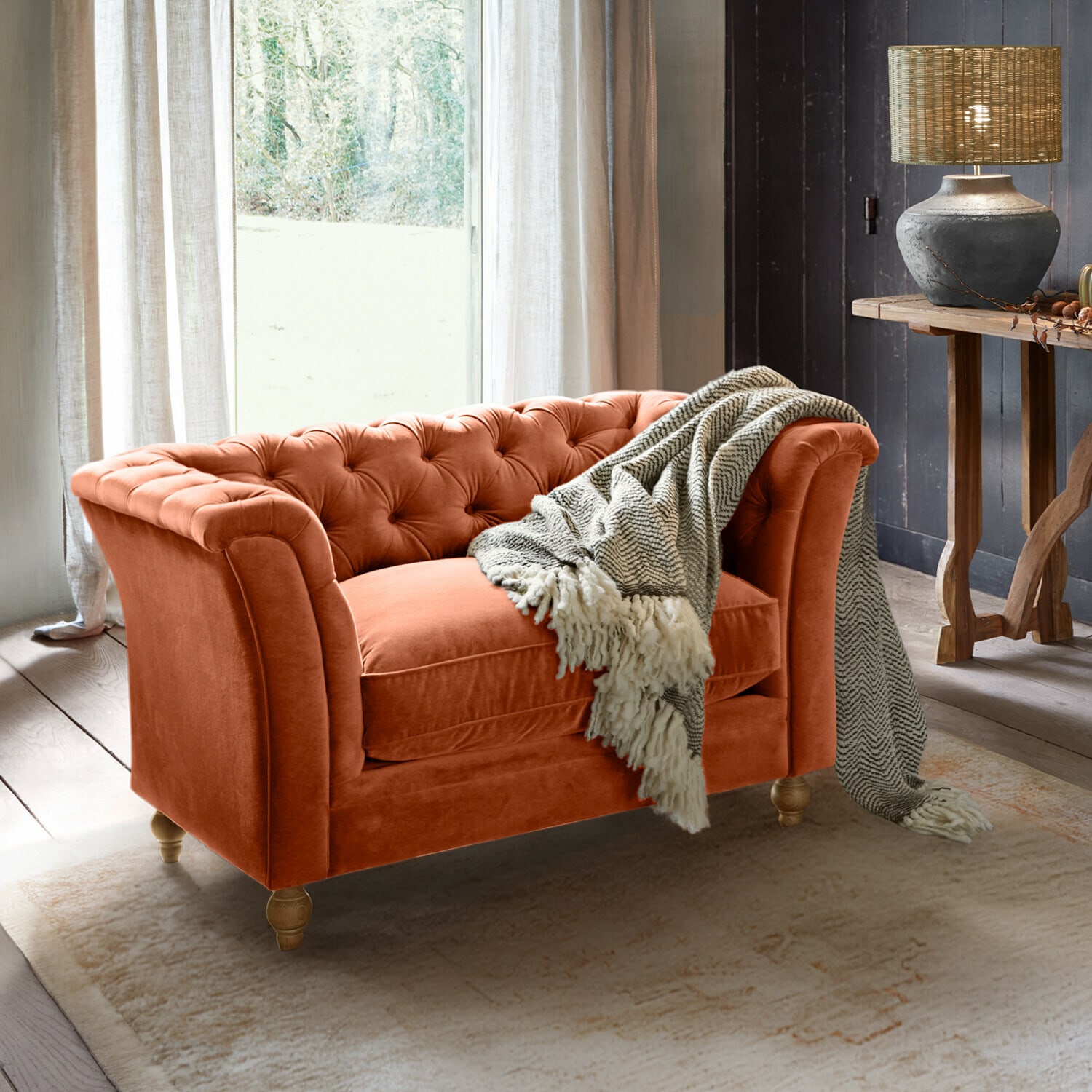 Pomarańczowa aksamitna sofa Chesterfield z szarym kocem w przytulnym salonie z lampą i drewnianym stołem