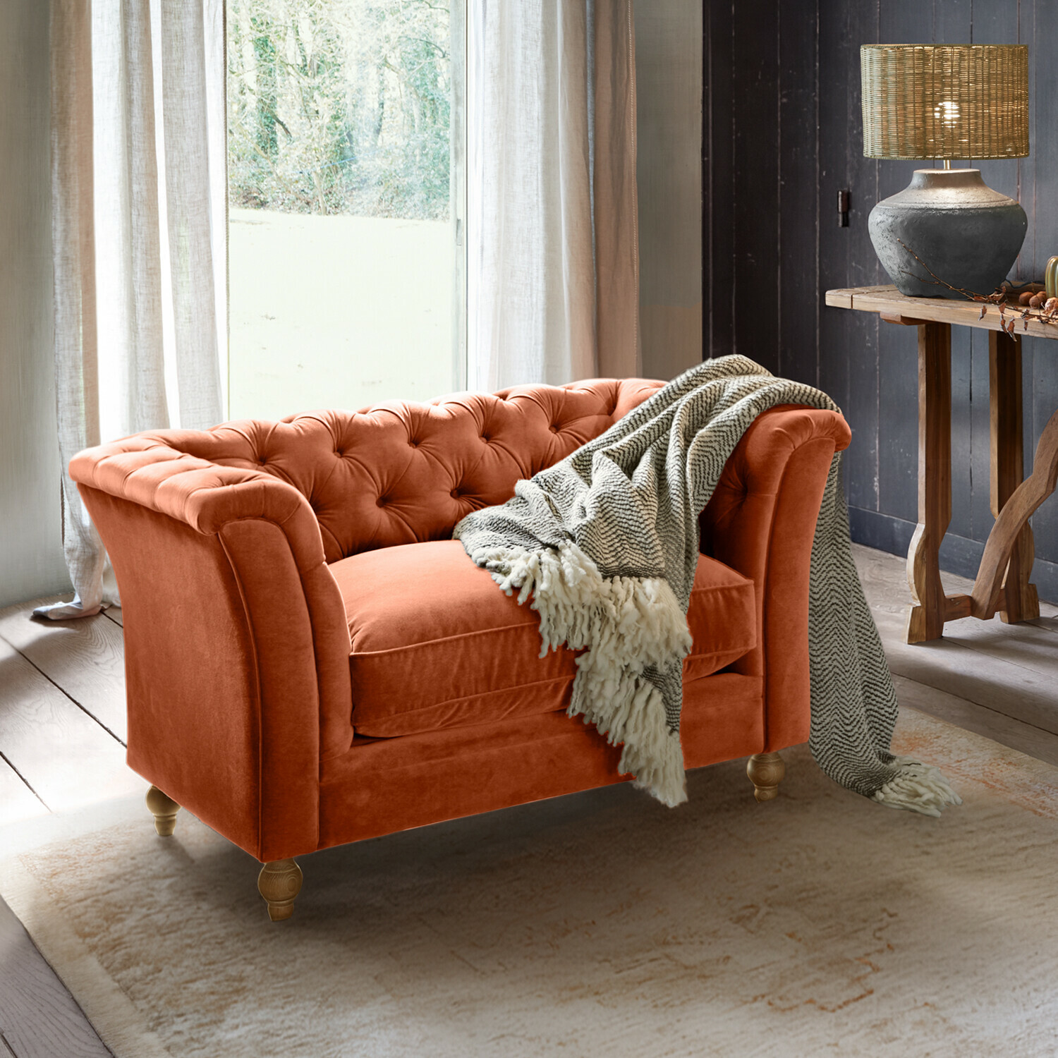 Sofa Clères Pomarańczowa aksamitna sofa Chesterfield z szarym kocem w przytulnym salonie z lampą i drewnianym stołem