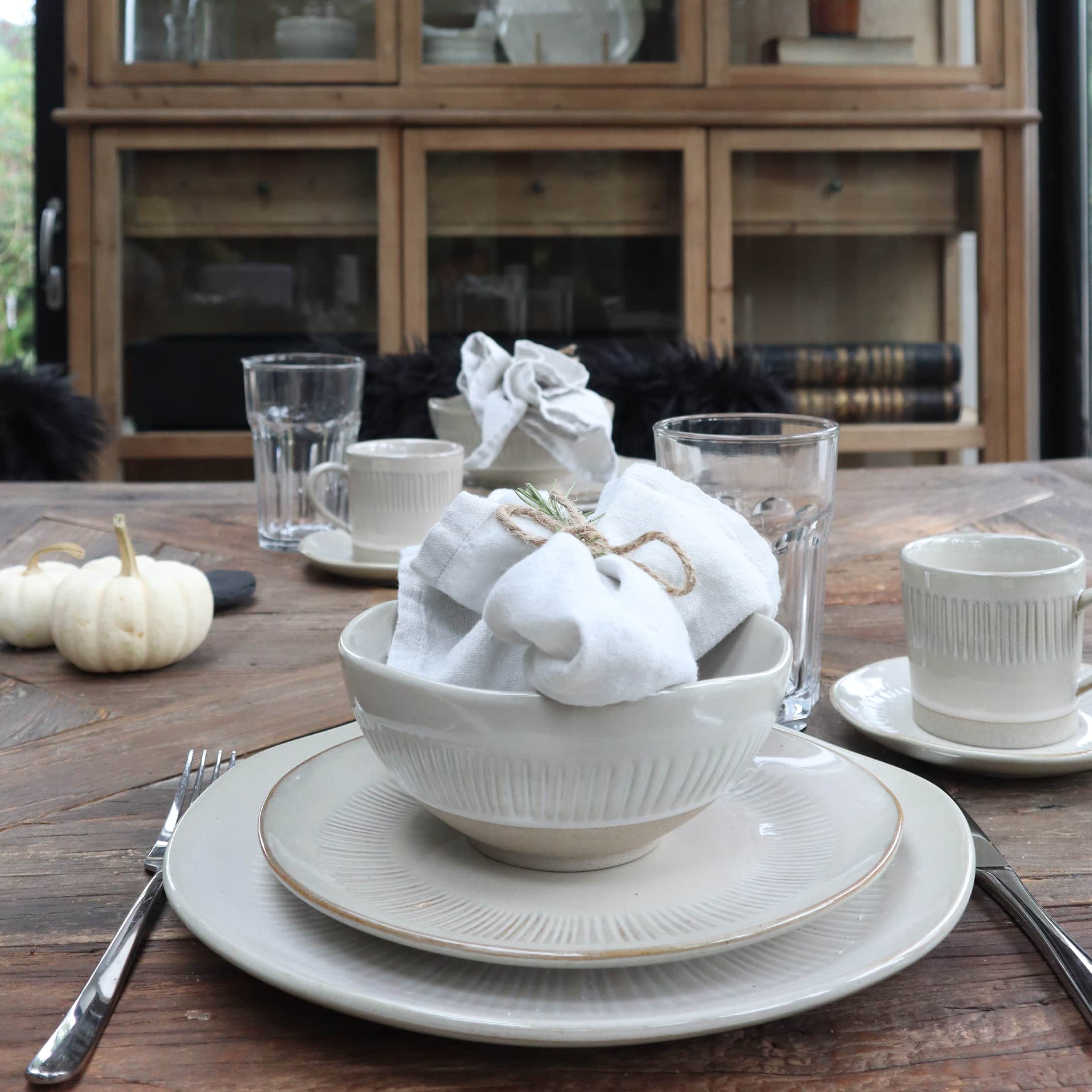 Zestaw kremowej ceramiki stołowej na drewnianym stole z białymi serwetkami i szklankami w stylu rustykalnym