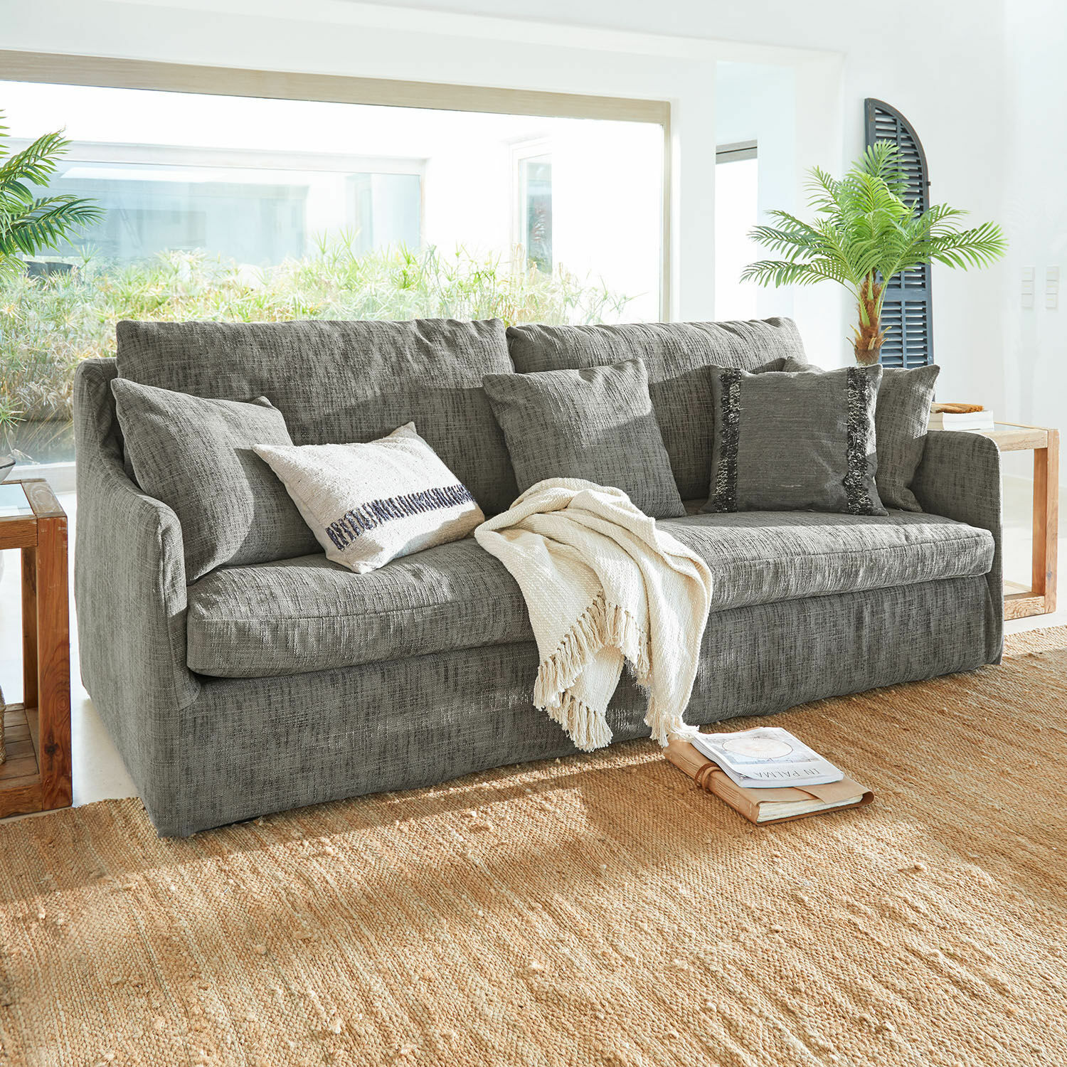 Sofa Shadowfield Szara sofa z tkaniny z poduszkami i kremowym kocem na naturalnym dywanie w jasnym salonie