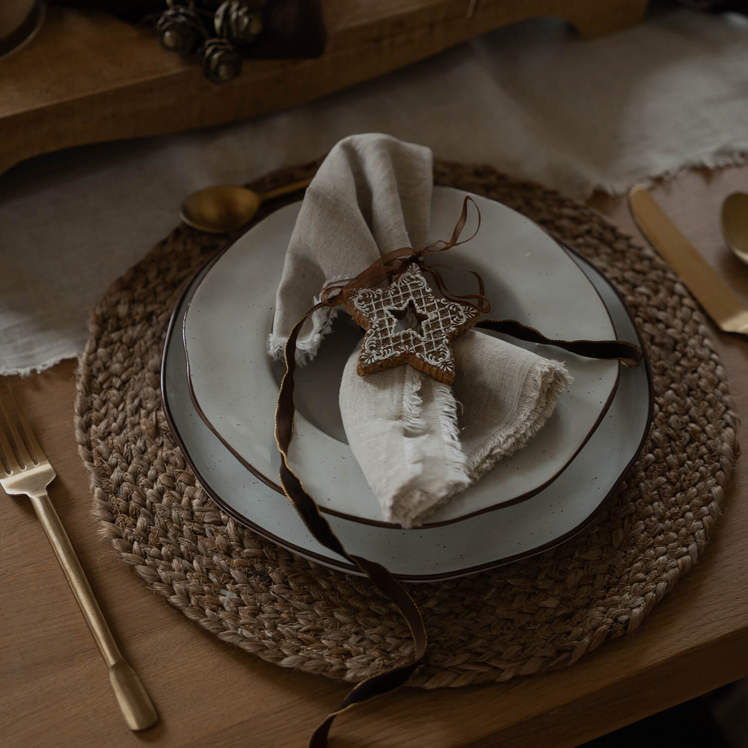 Rustykalny zestaw stołowy z ceramicznymi talerzami i lnianą serwetką ozdobioną gwiazdką piernikową