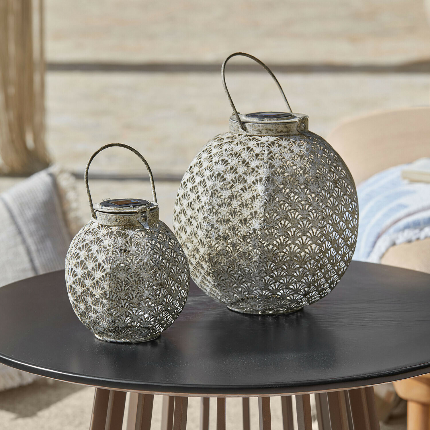 Lampion solarny, zestaw 2 szt. Omirah Dwie ażurowe lampiony z metalu w kolorze szarym na czarnym stole, dekoracja ogrodowa