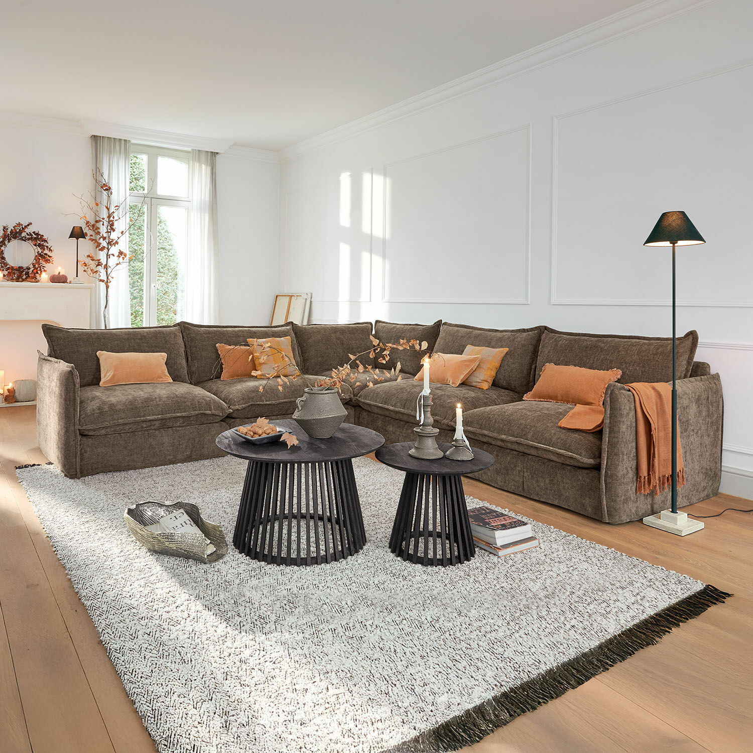 Sofa Illingworth Przytulny narożnik w brązowym materiale z pomarańczowymi poduszkami i czarnymi stolikami kawowymi w salonie