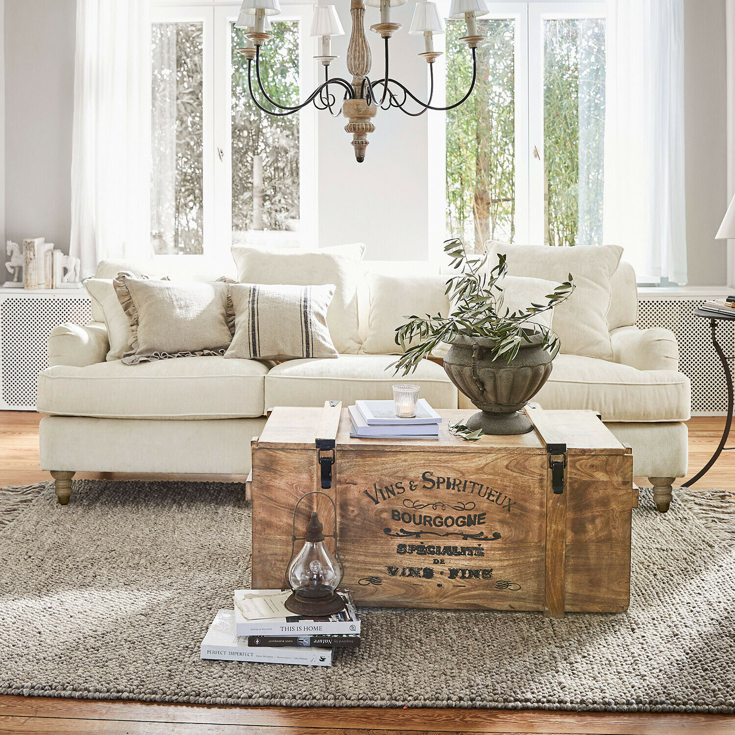 Sofa Isa Drewniana skrzynia z napisem vintage jako stolik kawowy w jasnym salonie z beżową sofą i dekoracją
