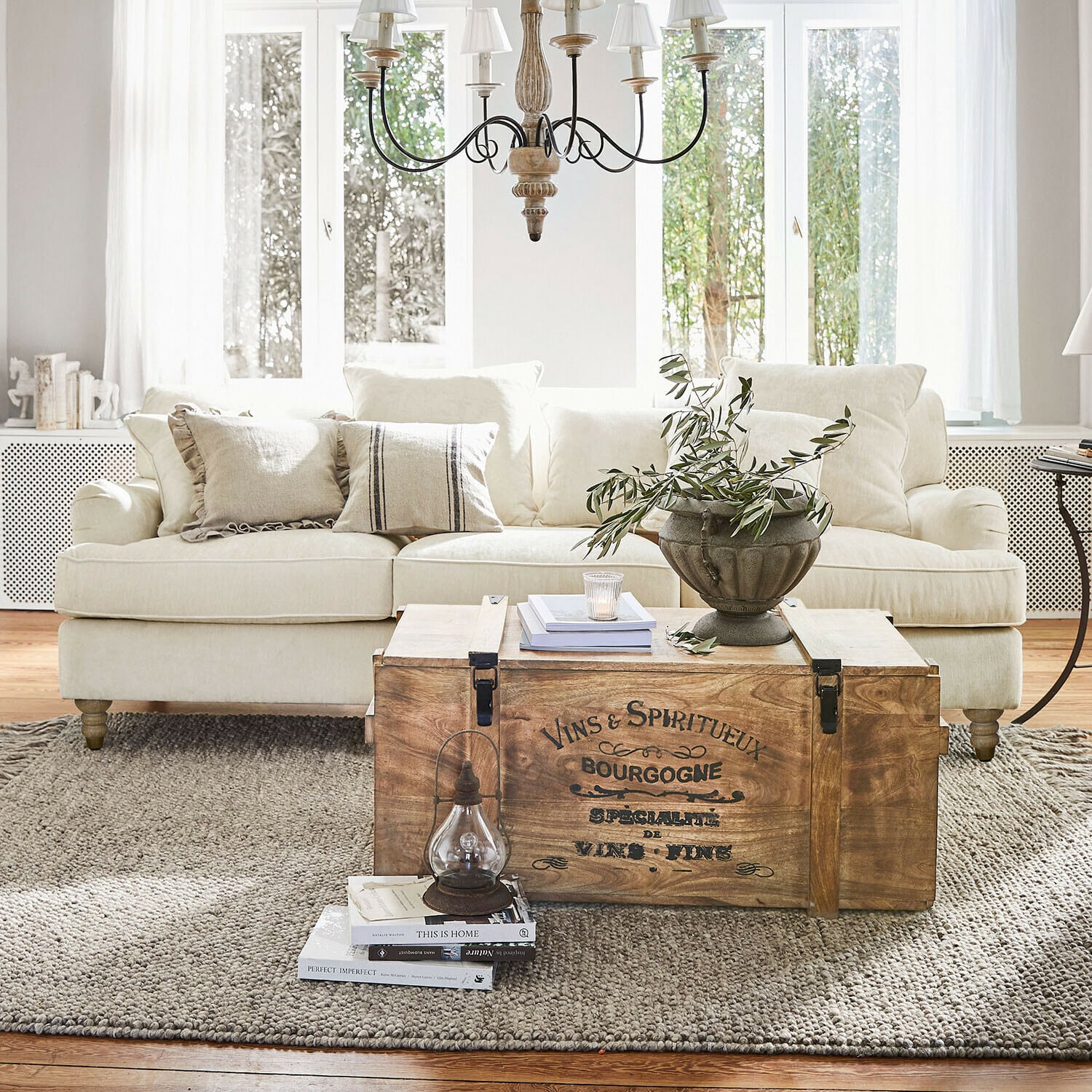 Sofa Isa Drewniana skrzynia z napisem vintage jako stolik kawowy w jasnym salonie z beżową sofą i dekoracją