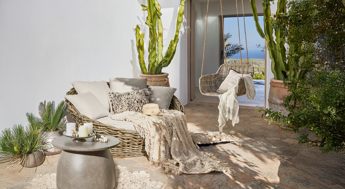 Przytulny zestaw mebli z rattanu w beżowych odcieniach na tarasie z widokiem na morze