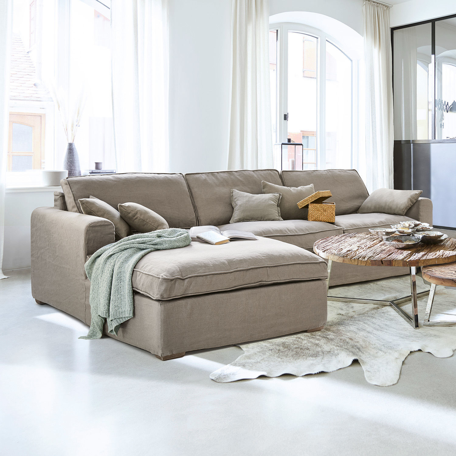 Sofa Seaford Beżowa sofa narożna z tkaniny w jasnym salonie z drewnianym stolikiem i dekoracjami
