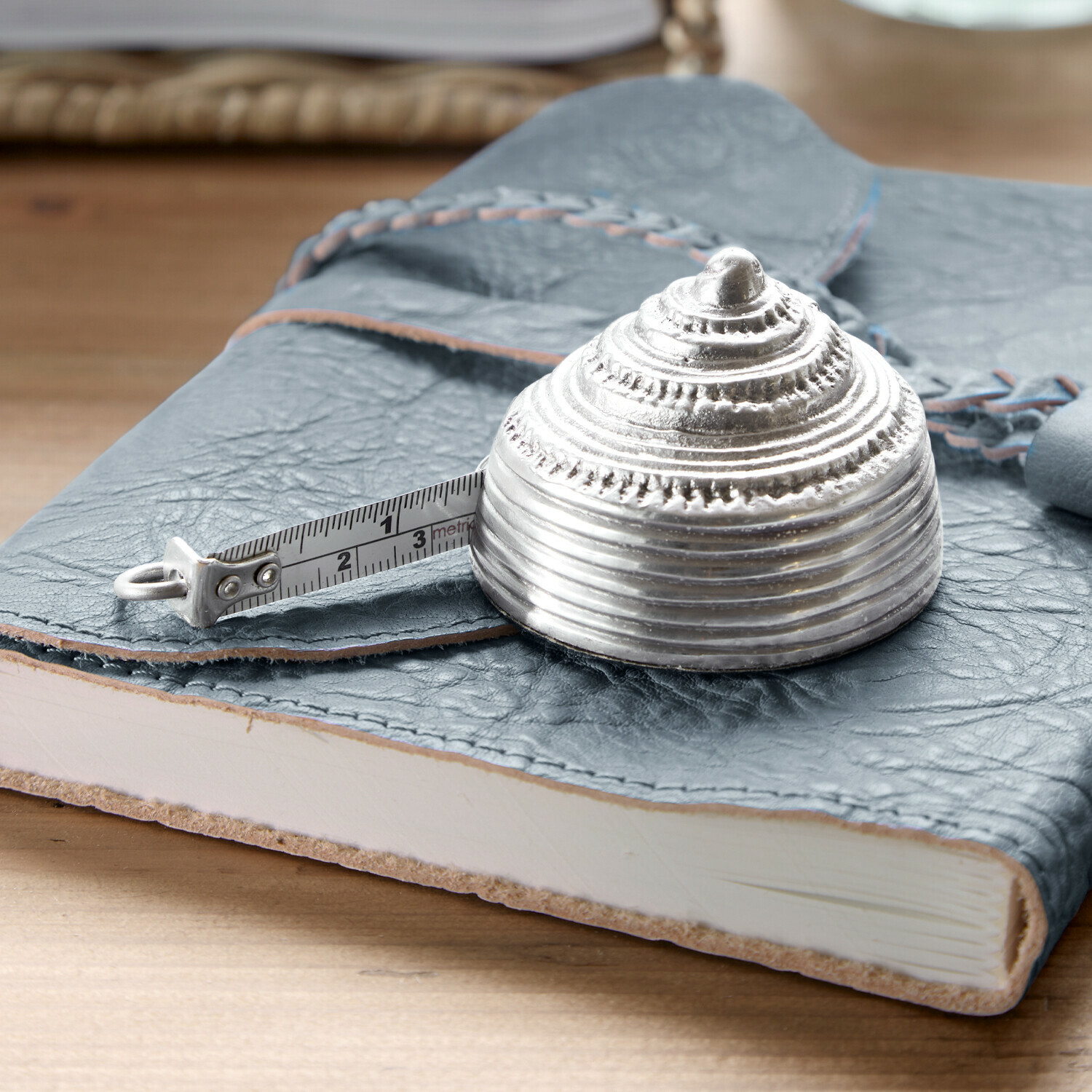 Metalowa, srebrna miarka zwijana w kształcie muszli na niebieskim skórzanym notesie