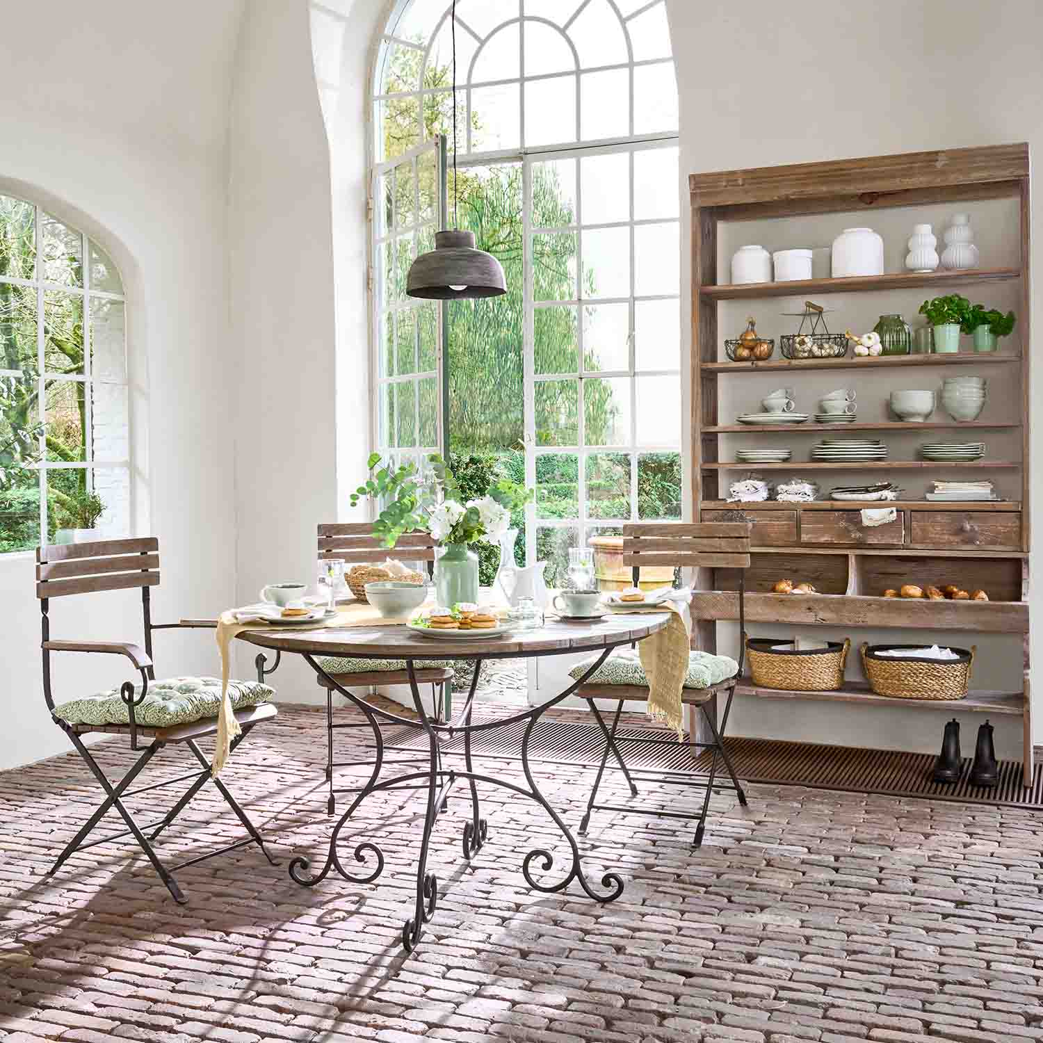 Jadalnia z okrągłym stołem z metalowymi nogami i drewnianymi krzesłami na ceglanej podłodze