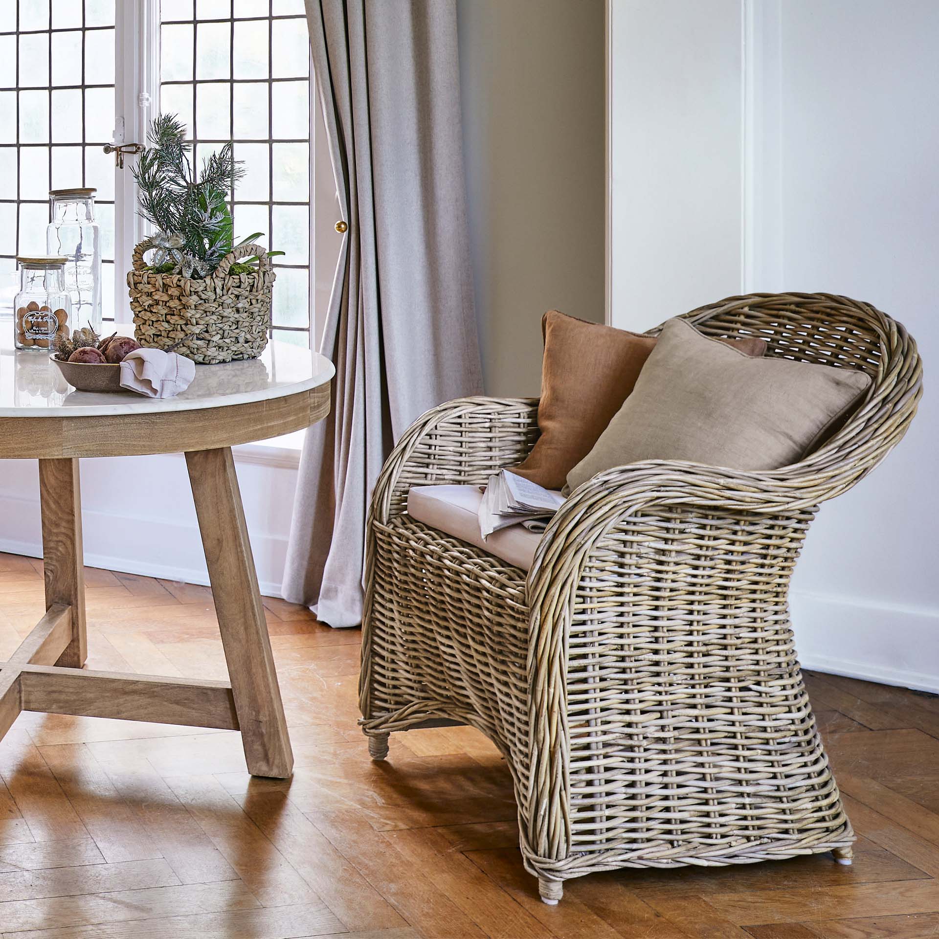 Naturalny rattanowy fotel z beżowymi poduszkami w jasnym salonie z drewnianą podłogą