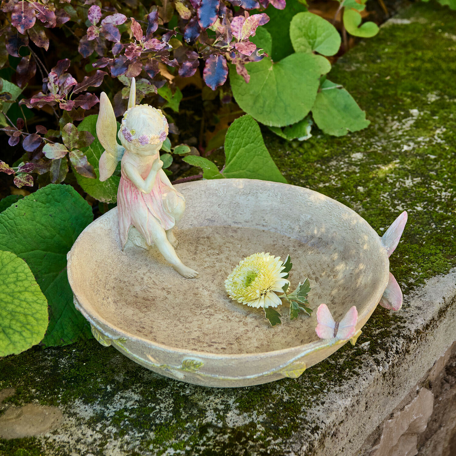 Ozdobna miska ogrodowa z figurką wróżki i motylami w pastelowych kolorach na kamiennym murze