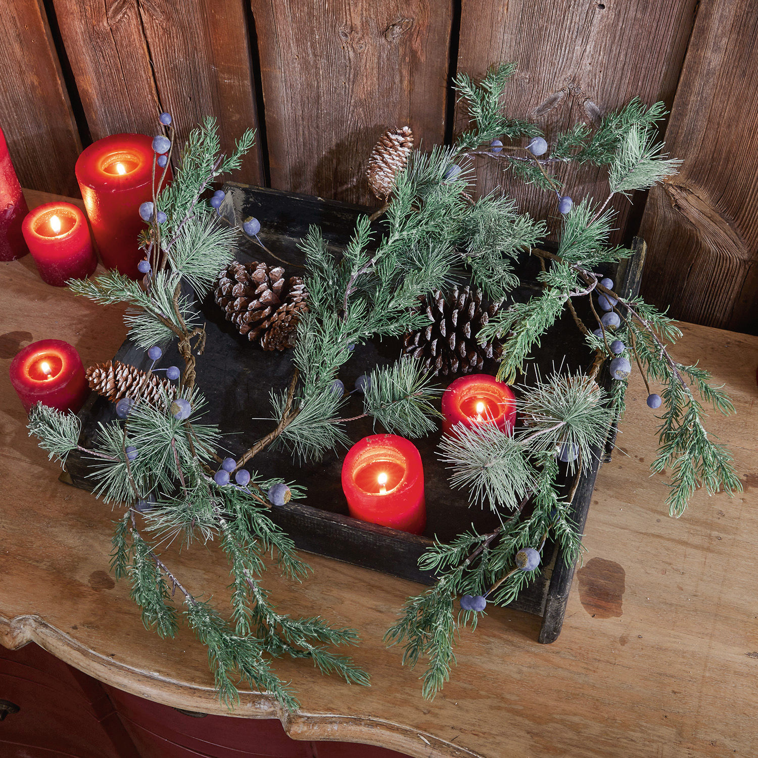 Girlanda Virpi Dekoracyjny wieniec z zielonych gałązek, szyszek i czerwonych świec na drewnianym stole