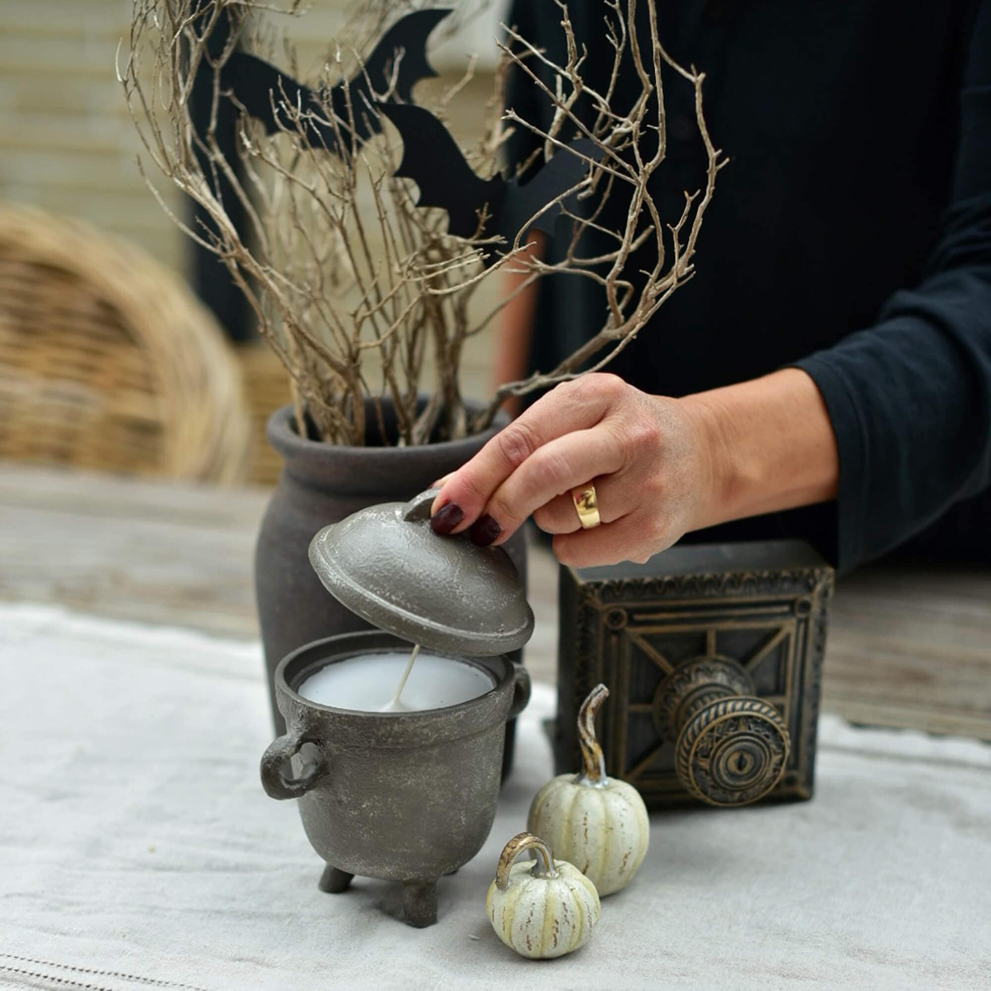 Szara świeca w kształcie kotła z pokrywką na halloweenowym stole z dekoracjami z dyni i gałęzi