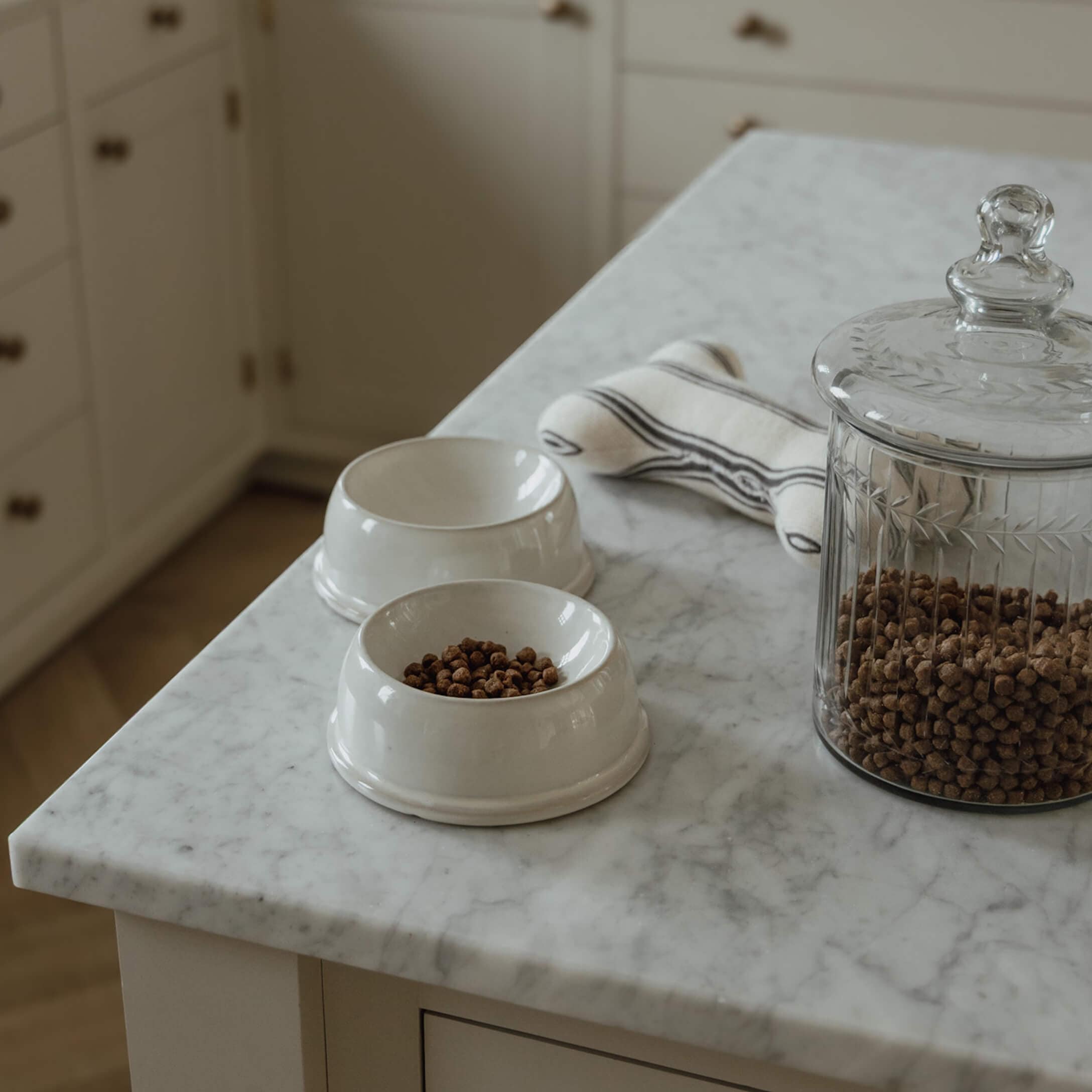 Białe ceramiczne miski na karmę z suchą karmą i szklany pojemnik na marmurowym blacie kuchennym