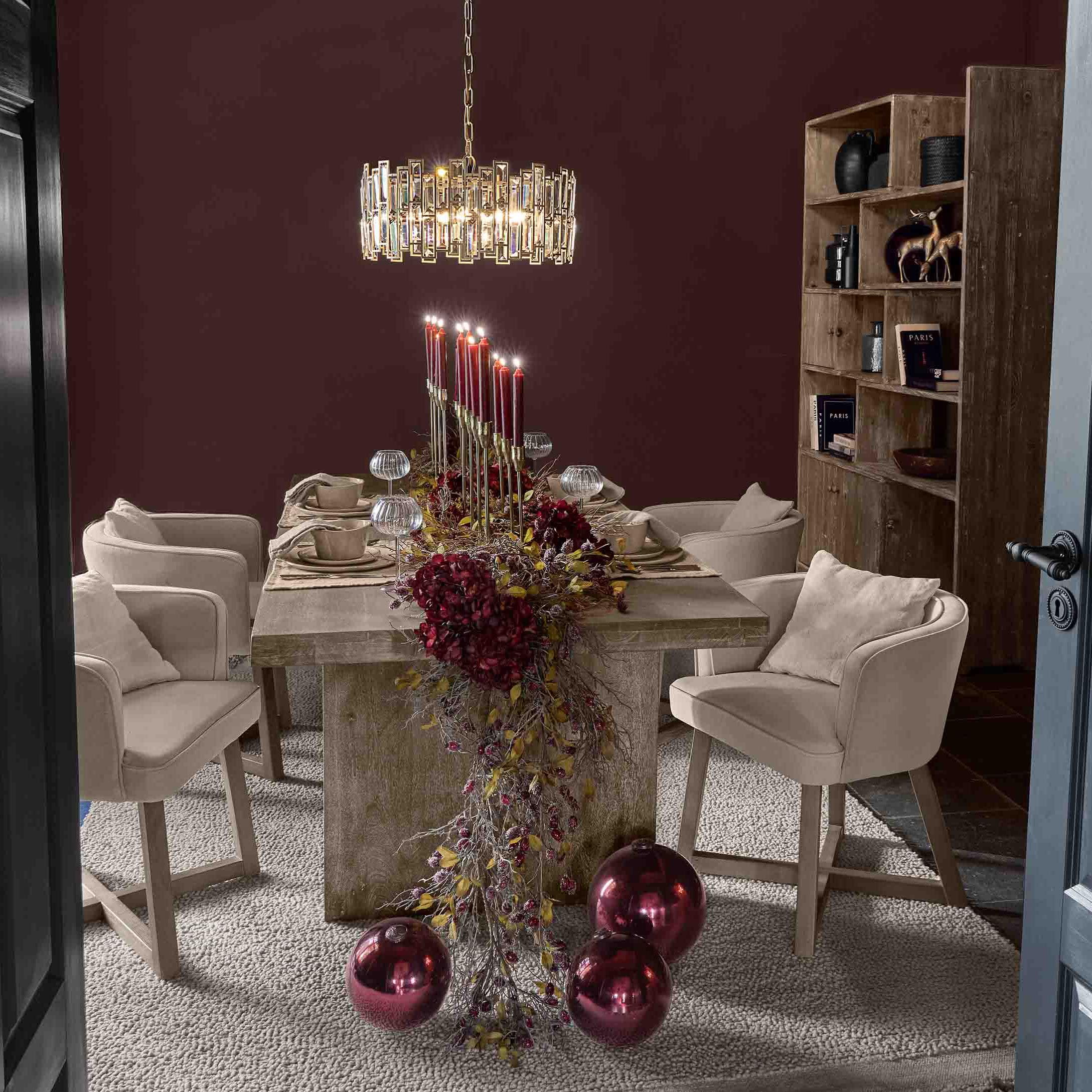 Jadalnia z drewnianym stołem, beżowymi krzesłami i dekoracją z czerwonych świec oraz bombek świątecznych