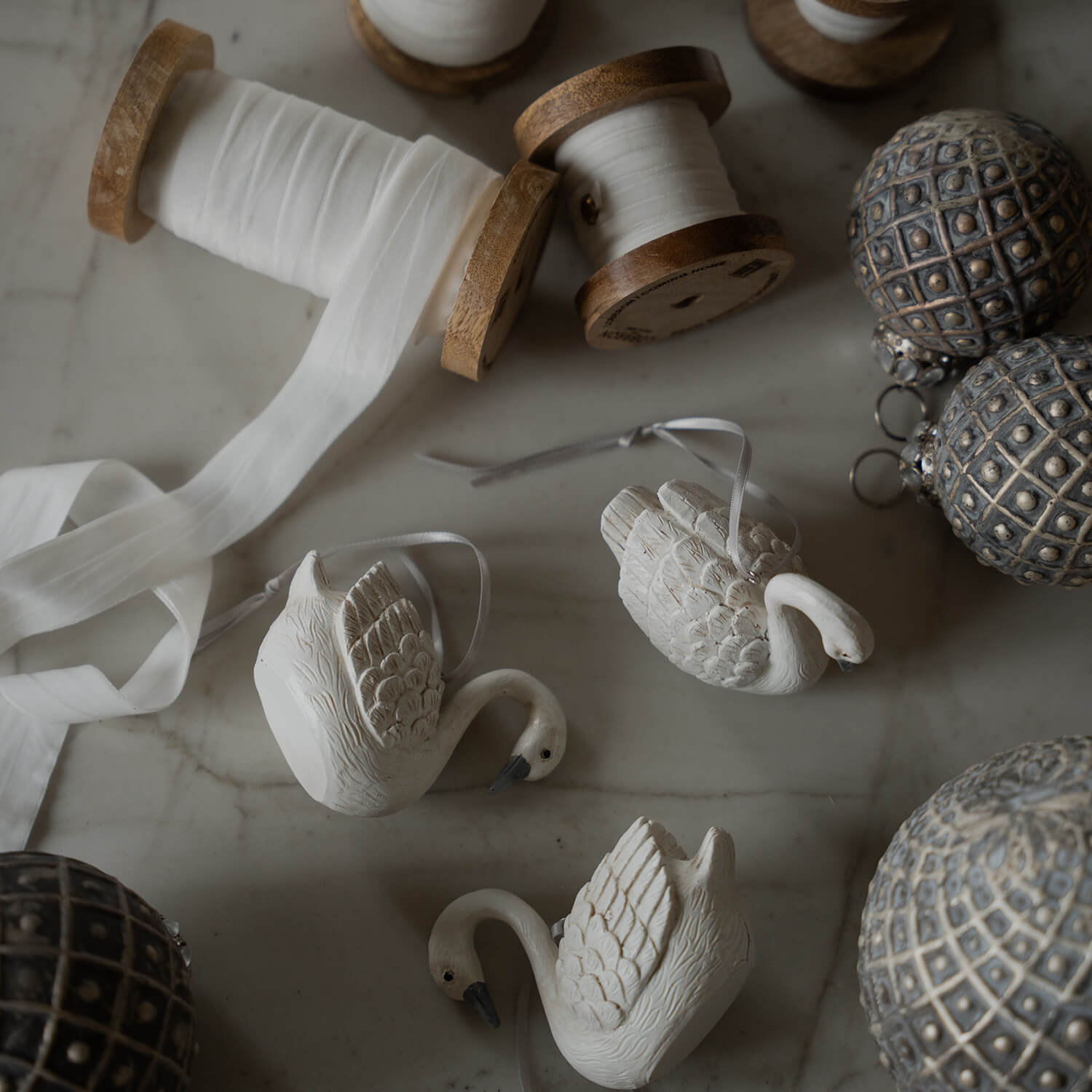 Białe ceramiczne ozdoby łabędzi z wstążką i drewniane szpule z białą wstążką na marmurowym stole