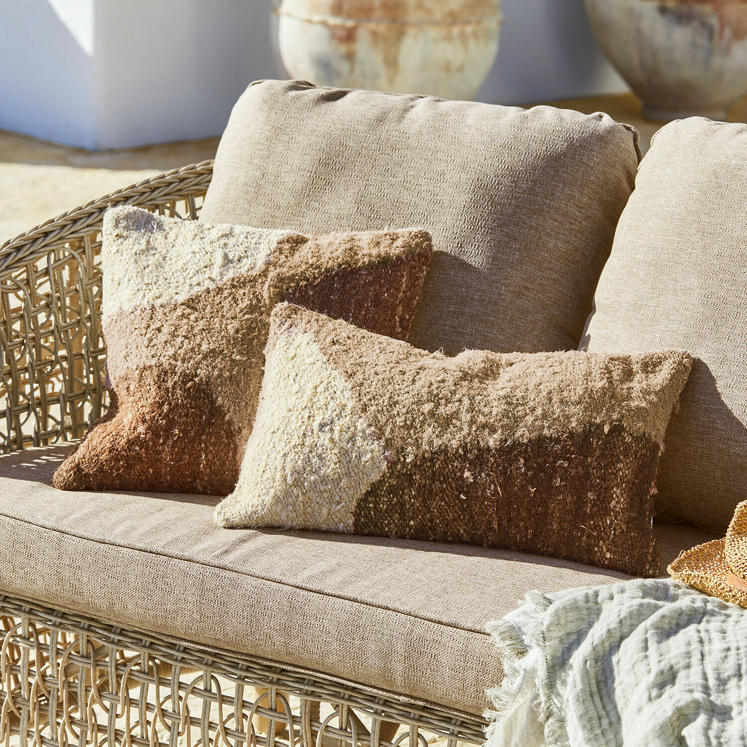 Beżowa sofa z wikliny z miękkimi poduszkami w odcieniach brązu i kremu, dekoracyjny tekstylny koc