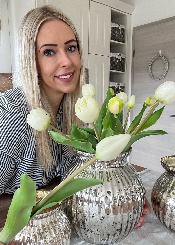 Kobieta z blond włosami obok srebrnej wazonu z białymi tulipanami w nowoczesnym wnętrzu