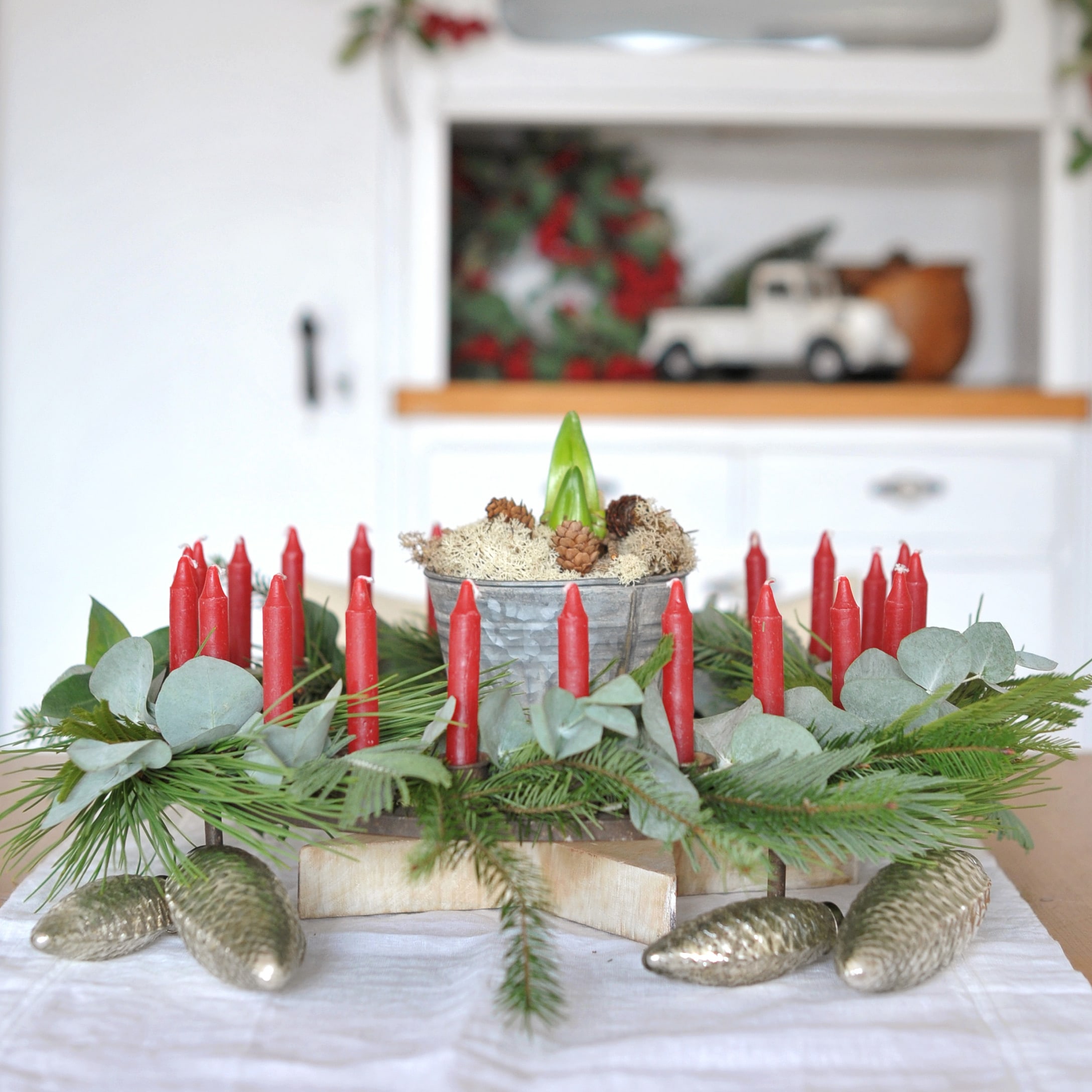 Dekoracyjny wieniec adwentowy z czerwonymi świecami, zielonymi gałązkami i metalowymi szyszkami na stole