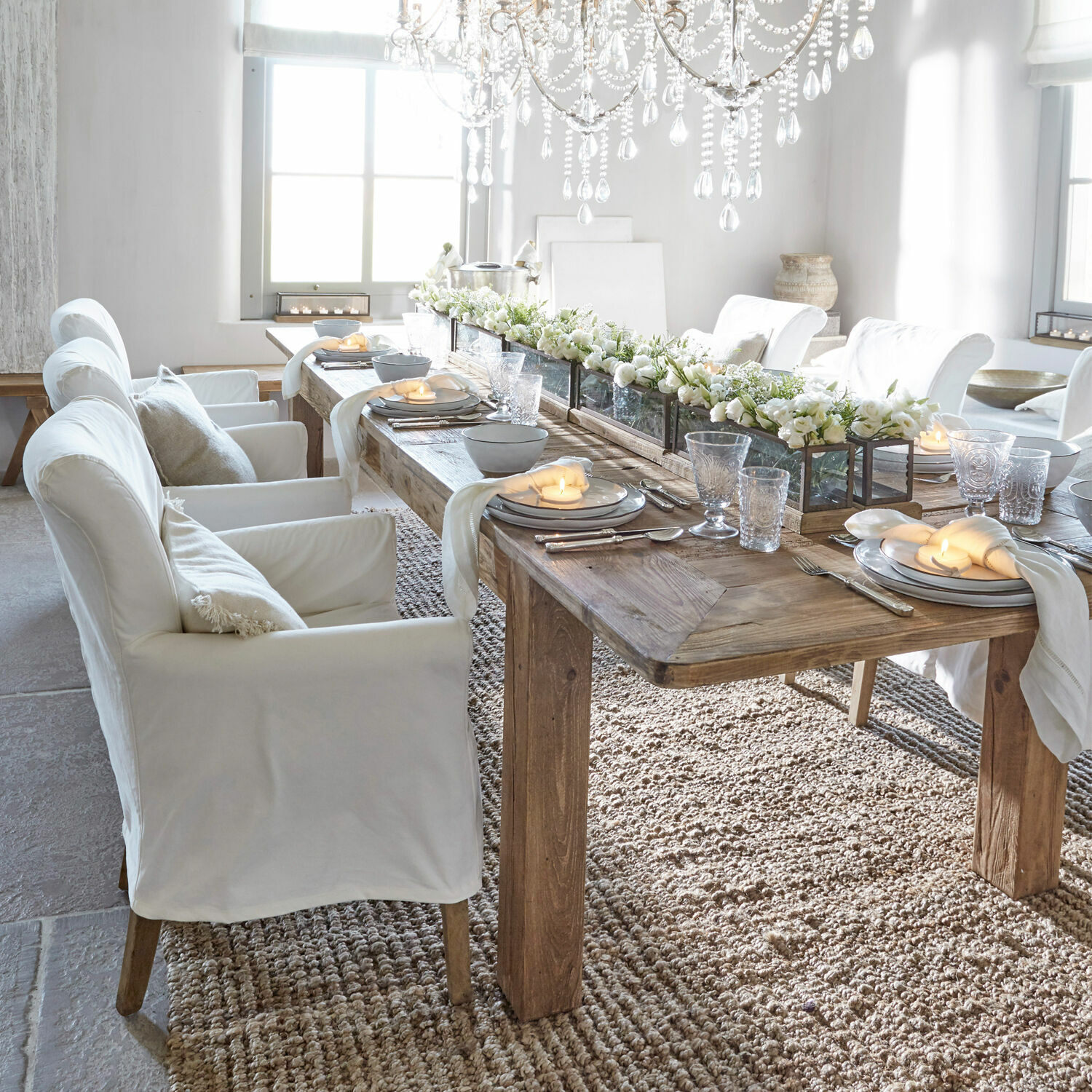Jadalnia z drewnianym stołem i białymi obitymi krzesłami, dekoracje kwiatowe i świece