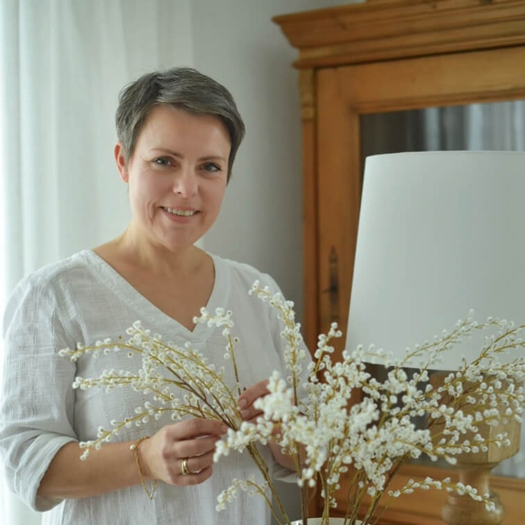 Kobieta w białej bluzce trzymająca dekoracyjne gałązki z białymi kwiatami w jasnym wnętrzu