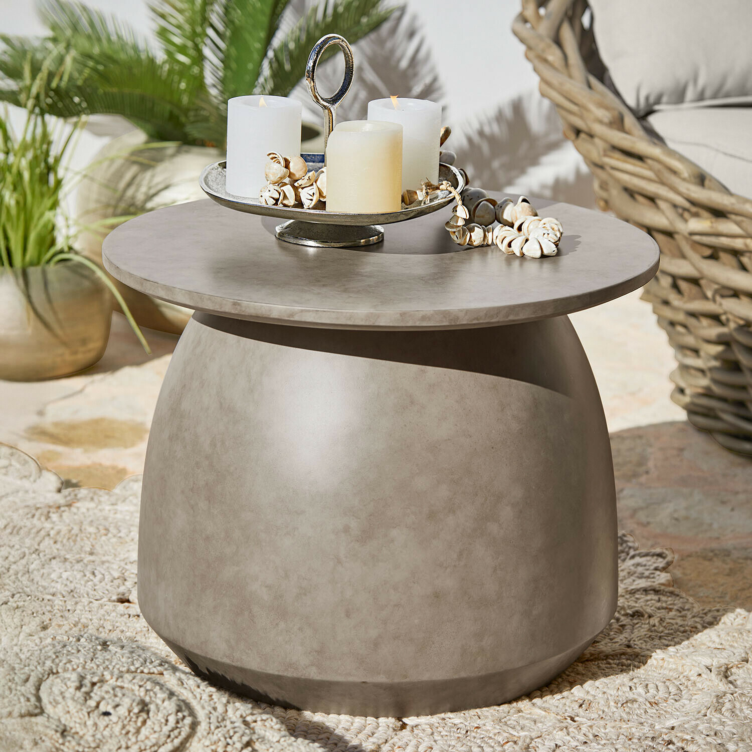 Okrągły stolik kawowy z betonu w szarym kolorze na taras z dekoracją świec i muszli