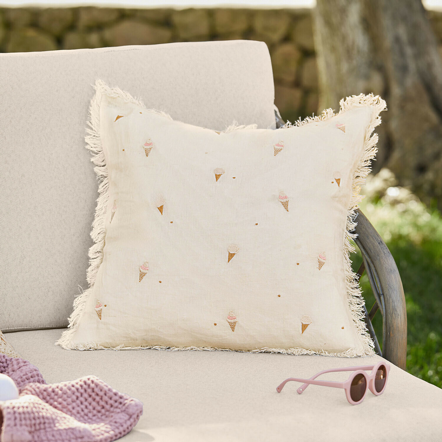 Beżowa lniana poduszka z frędzlami i wzorem lodów w rożkach na jasnej sofie w ogrodzie