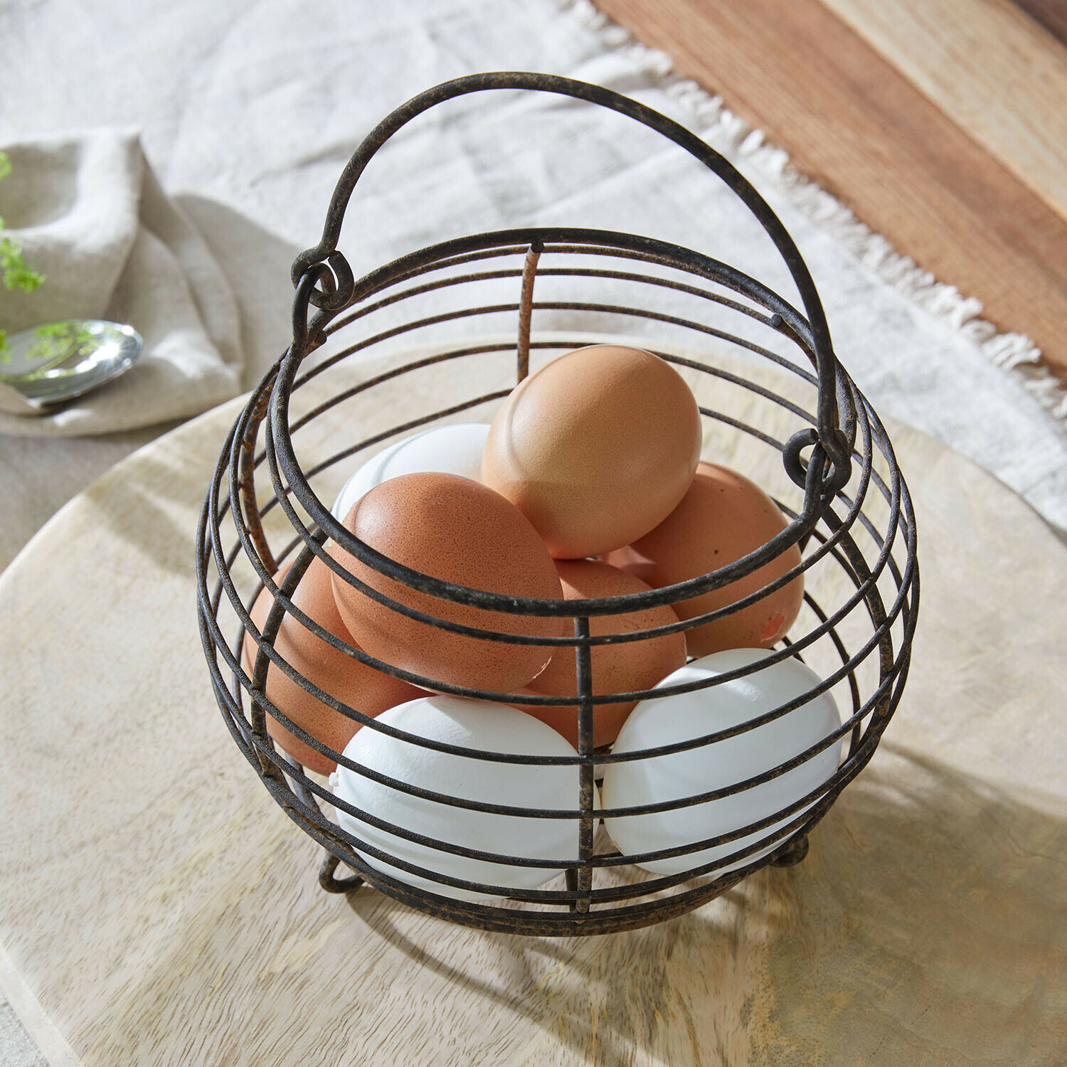 Metalowy koszyk na jajka w stylu vintage z brązowymi i białymi jajkami na drewnianej powierzchni