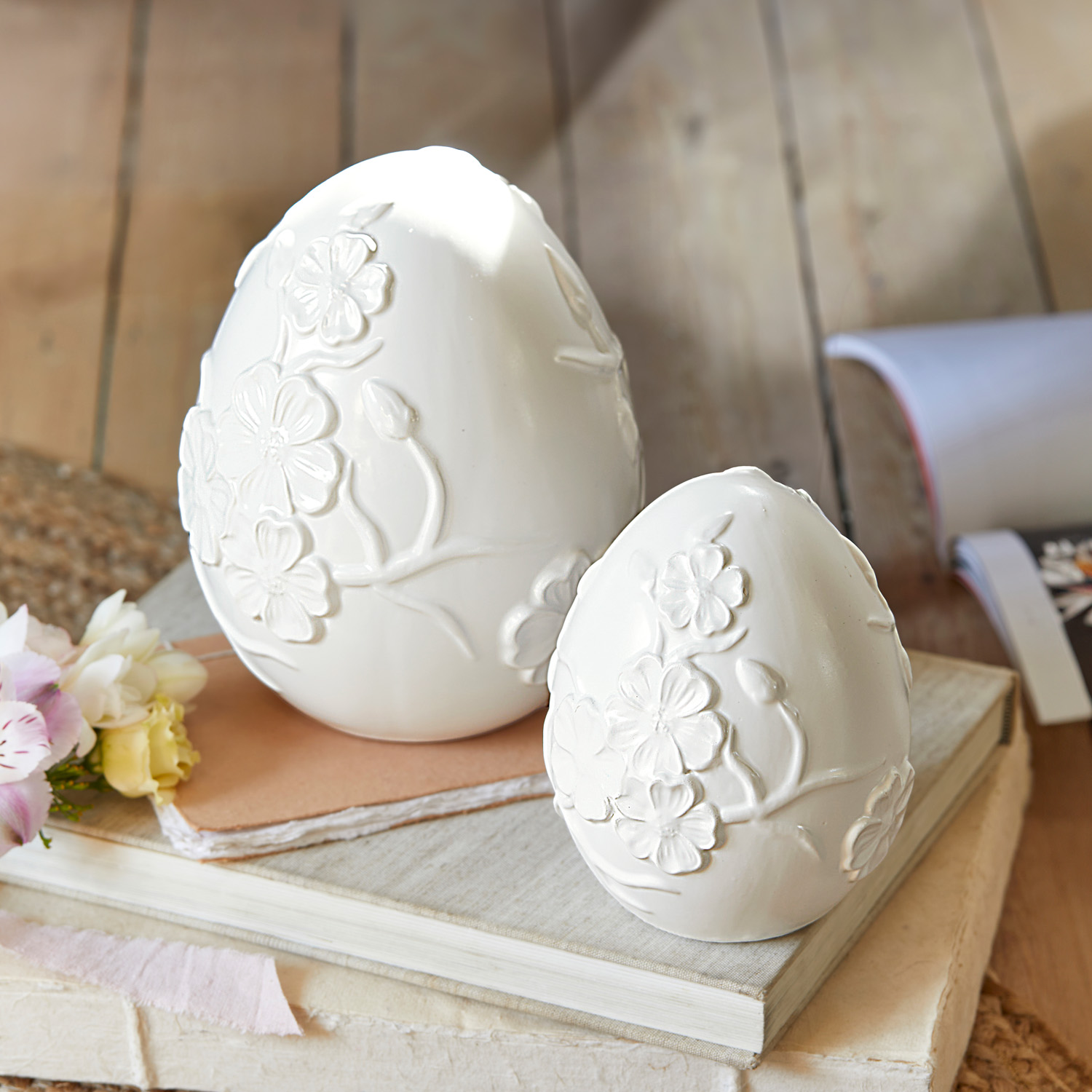 Białe ceramiczne dekoracyjne jajka z reliefem kwiatowym na książkach, ozdoba wiosenna